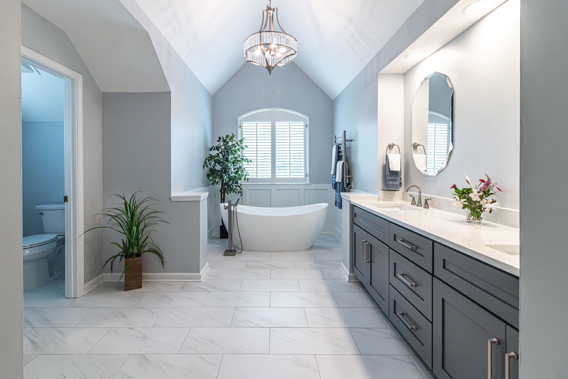 Bright modern bathroom with white tub, gray vanity, skylight, and tiled floor