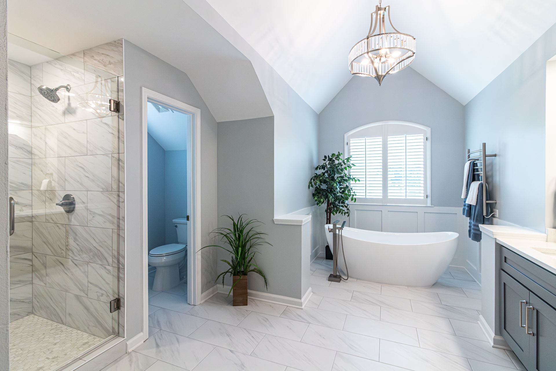 Bright blue-and-gray bathroom with a freestanding tub, glass shower, vanity, and white tile floor
