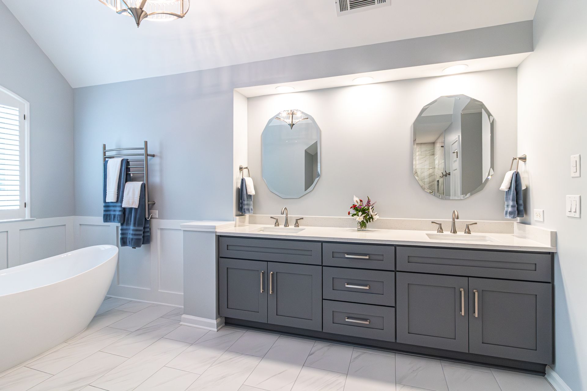 Bright bathroom with double vanity, two round mirrors, and a freestanding tub by a window.
