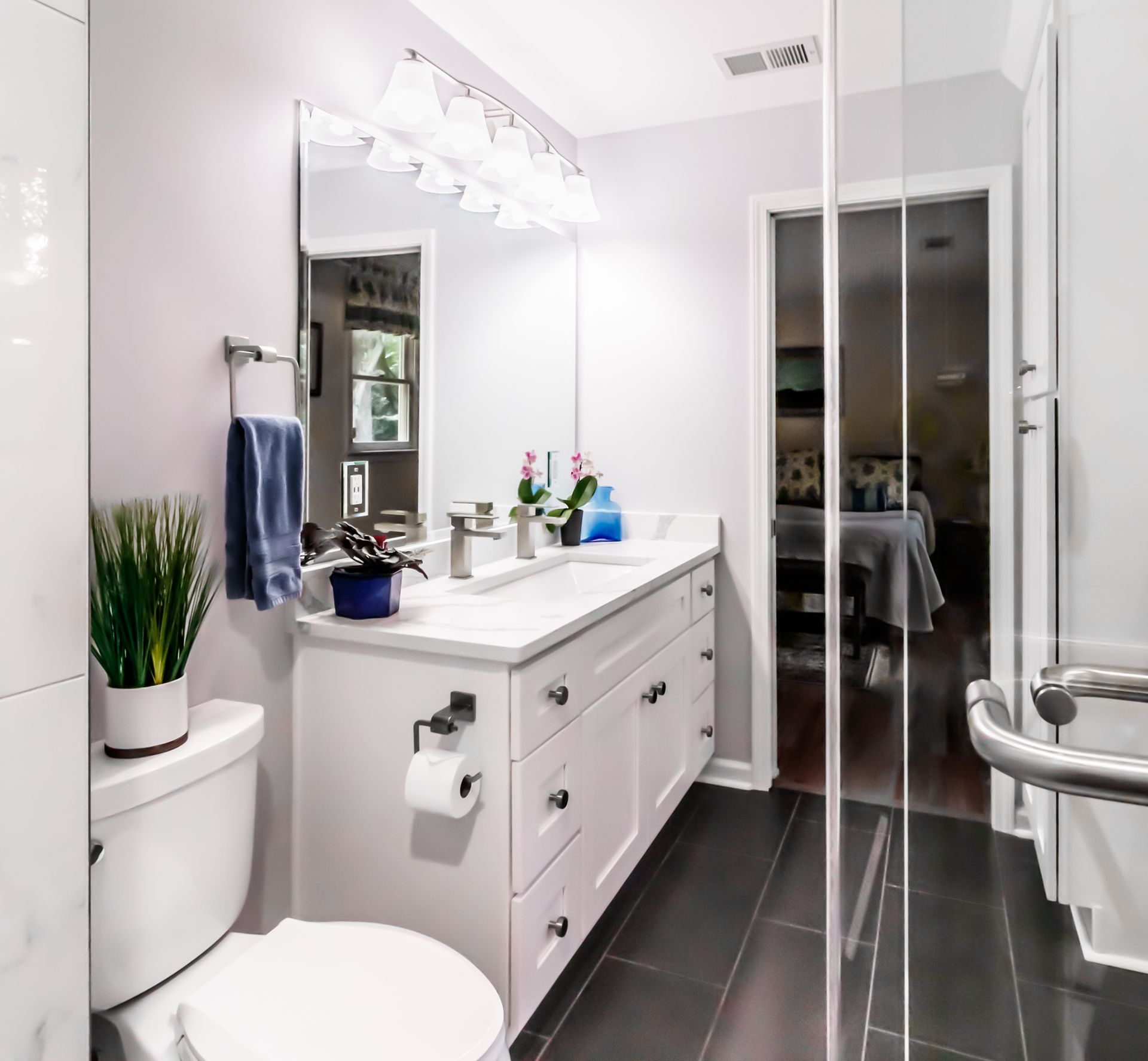 Bright modern bathroom with white vanity, black tile floor, glass shower, and toilet
