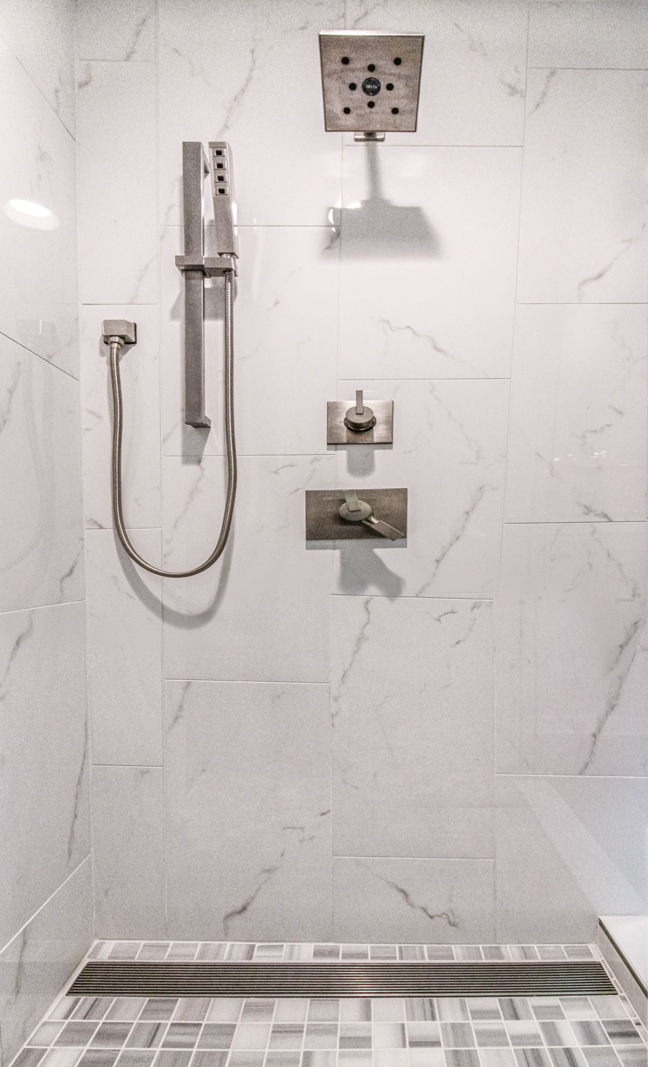 Modern shower with marble-tile wall, handheld showerhead, and built-in niche shelf.