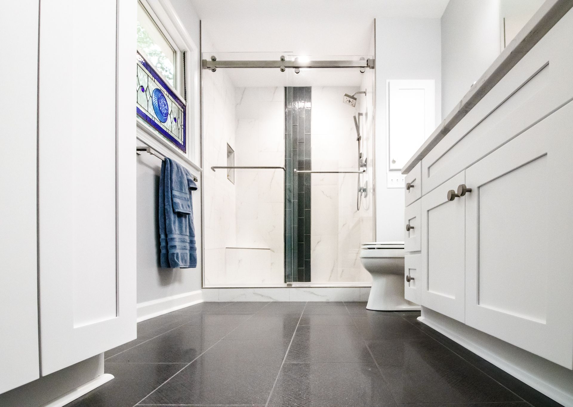 Bright modern bathroom with dark tile floor, glass shower, white vanity, and towel rack