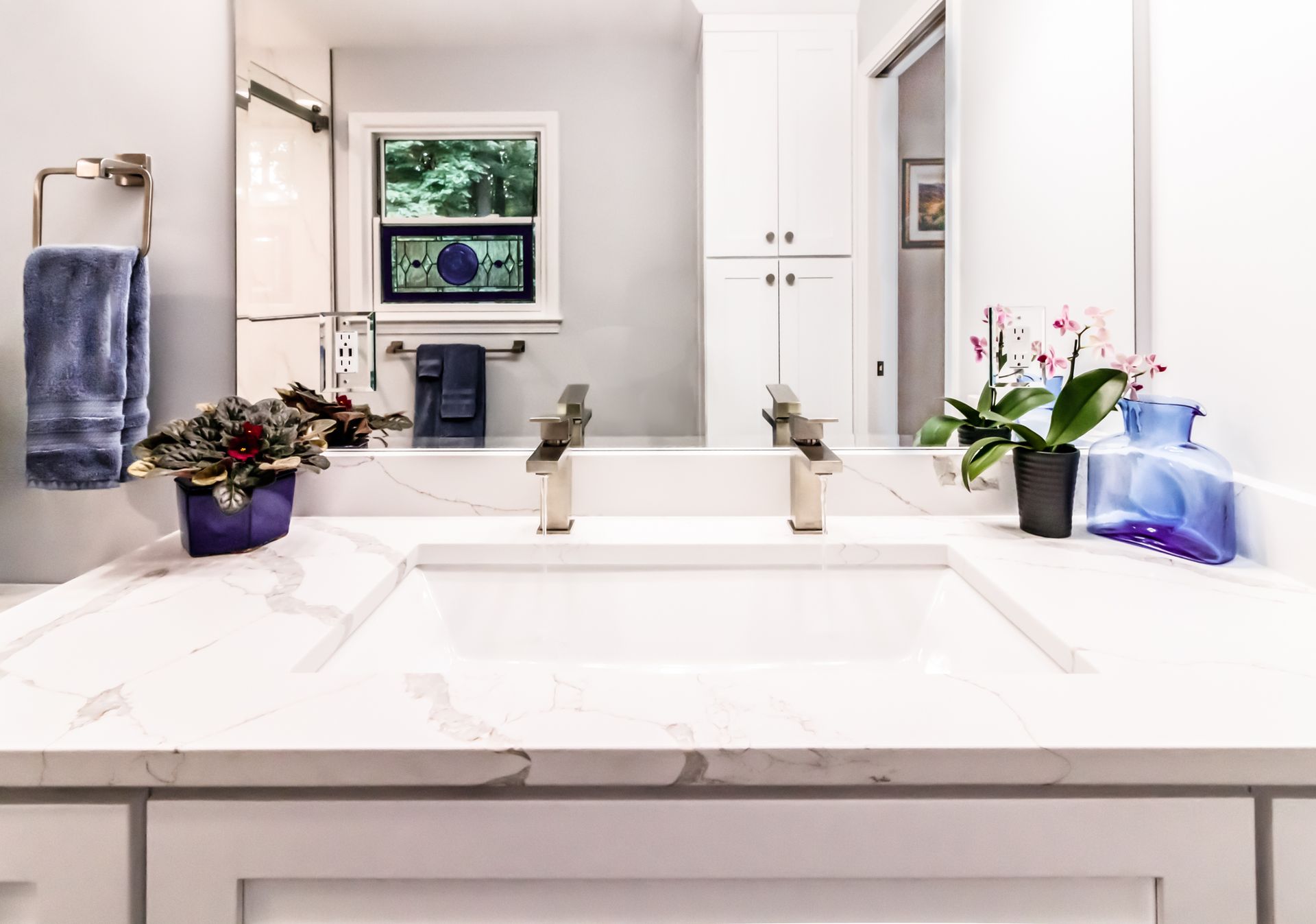 Bright bathroom vanity with double sink, large mirror, and potted flowers on the counter