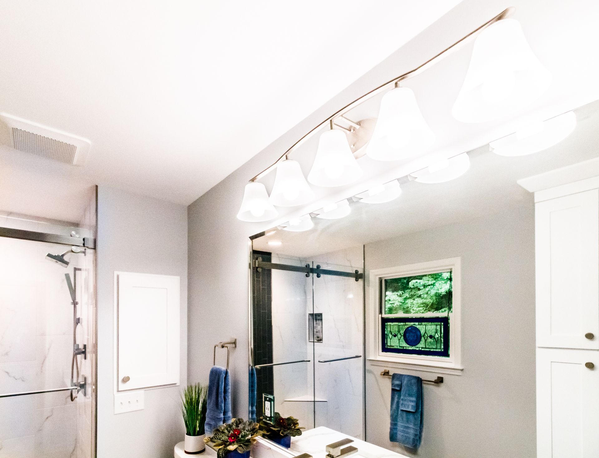 Bright bathroom with vanity lights, mirror, shower door, and white cabinets