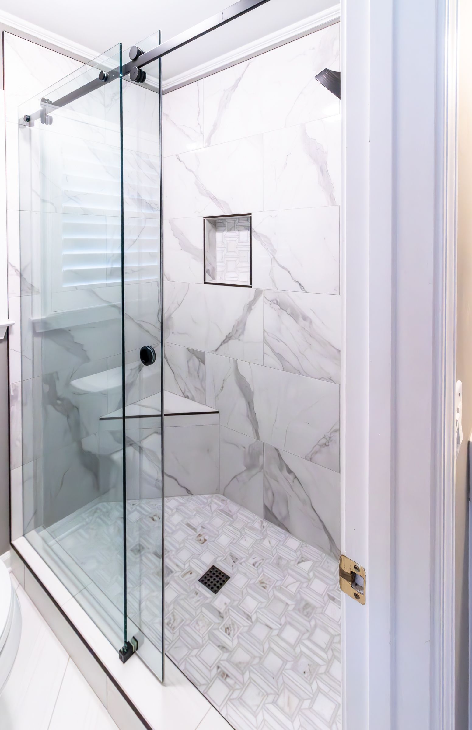 Modern glass shower with white marble tile and built-in niche in a bathroom