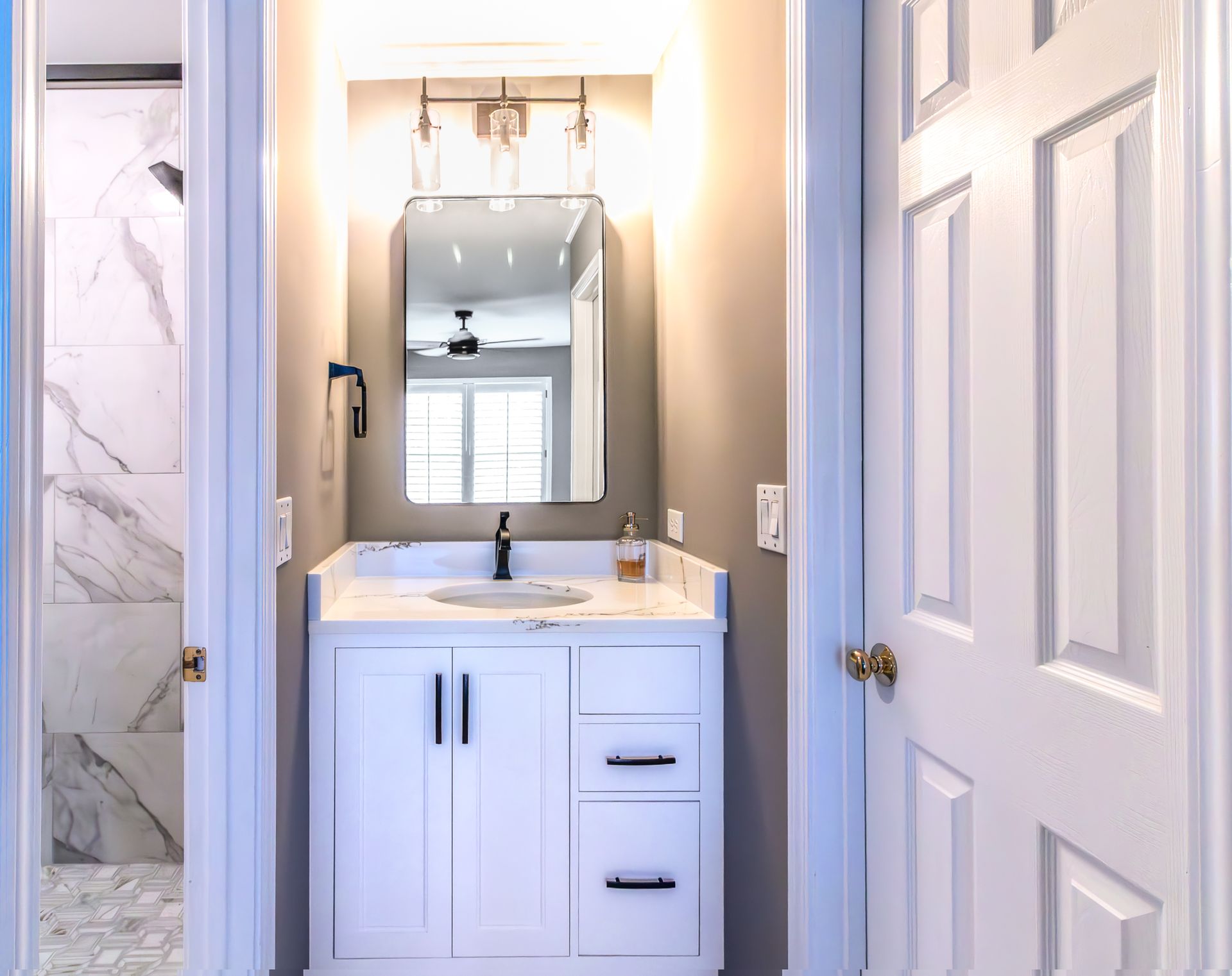 Small bathroom vanity with mirror, sink, and white cabinets, viewed through an open doorway