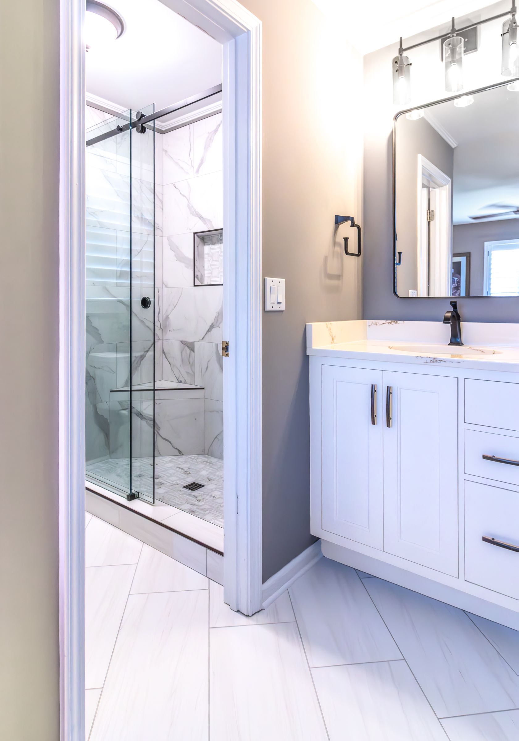 Bright white bathroom with glass-enclosed shower and vanity with mirror sink at right