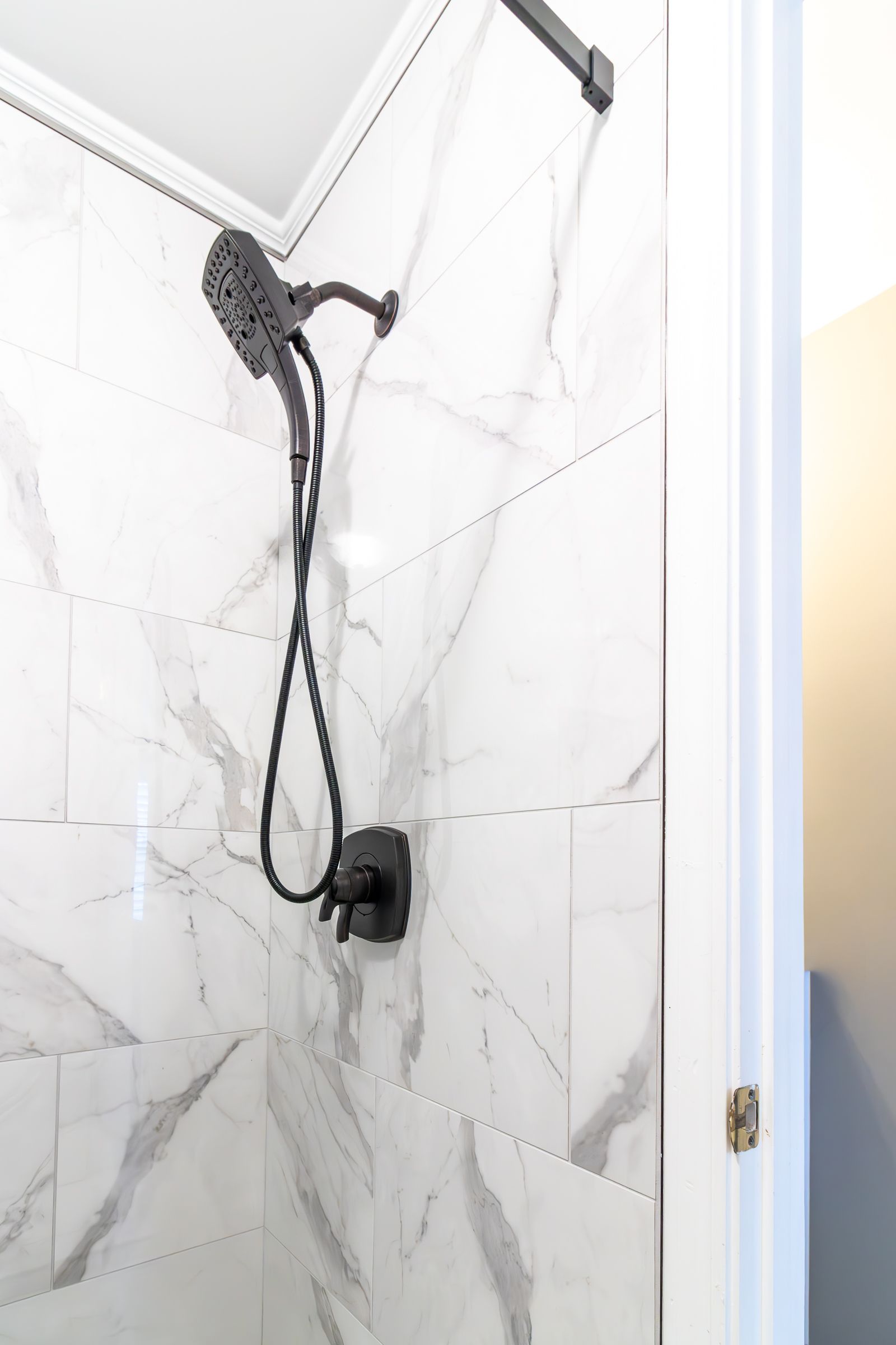 Black shower head with handheld hose on white tiled bathroom wall