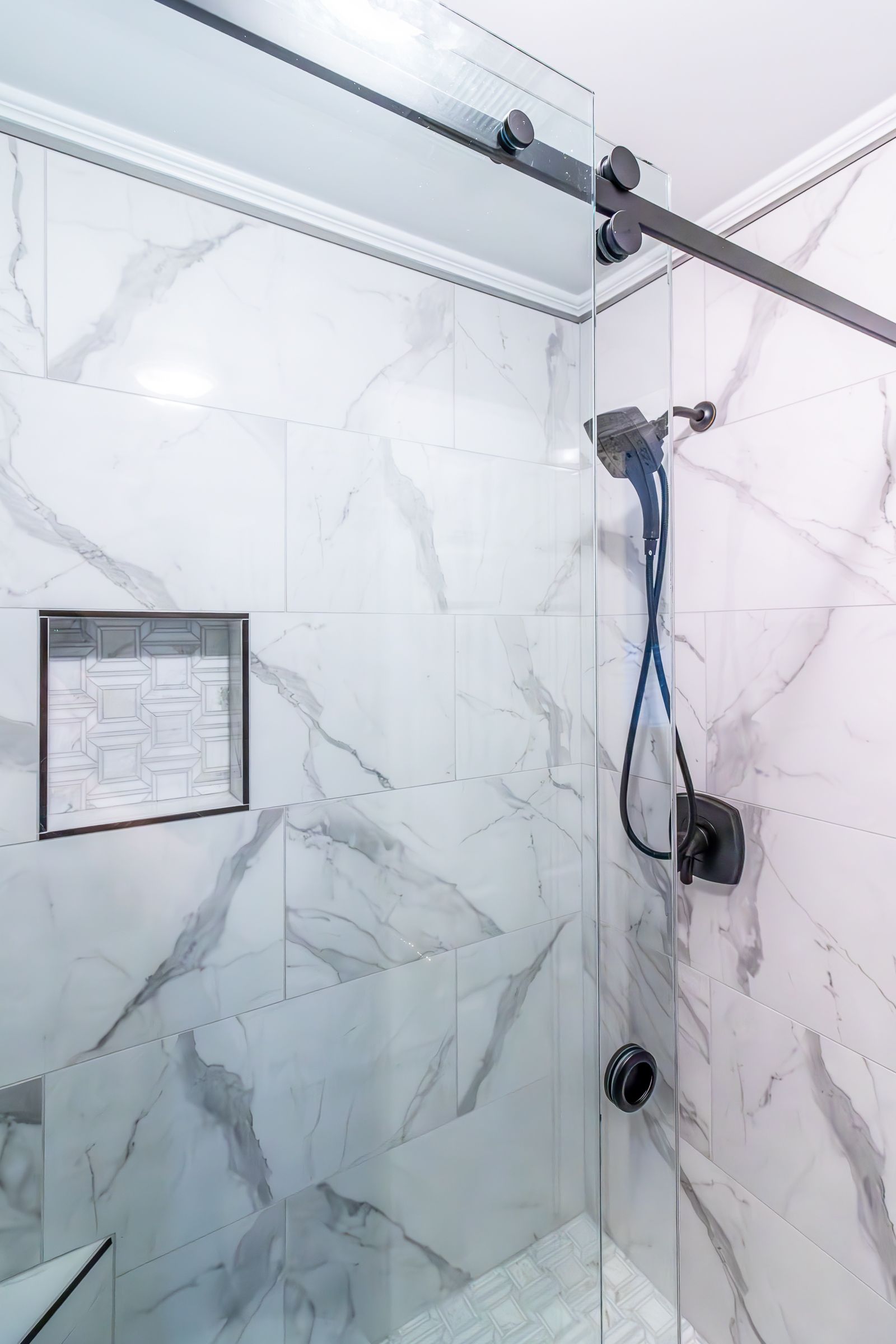 Modern tiled shower with glass door, chrome showerhead, and wall-mounted shower controls