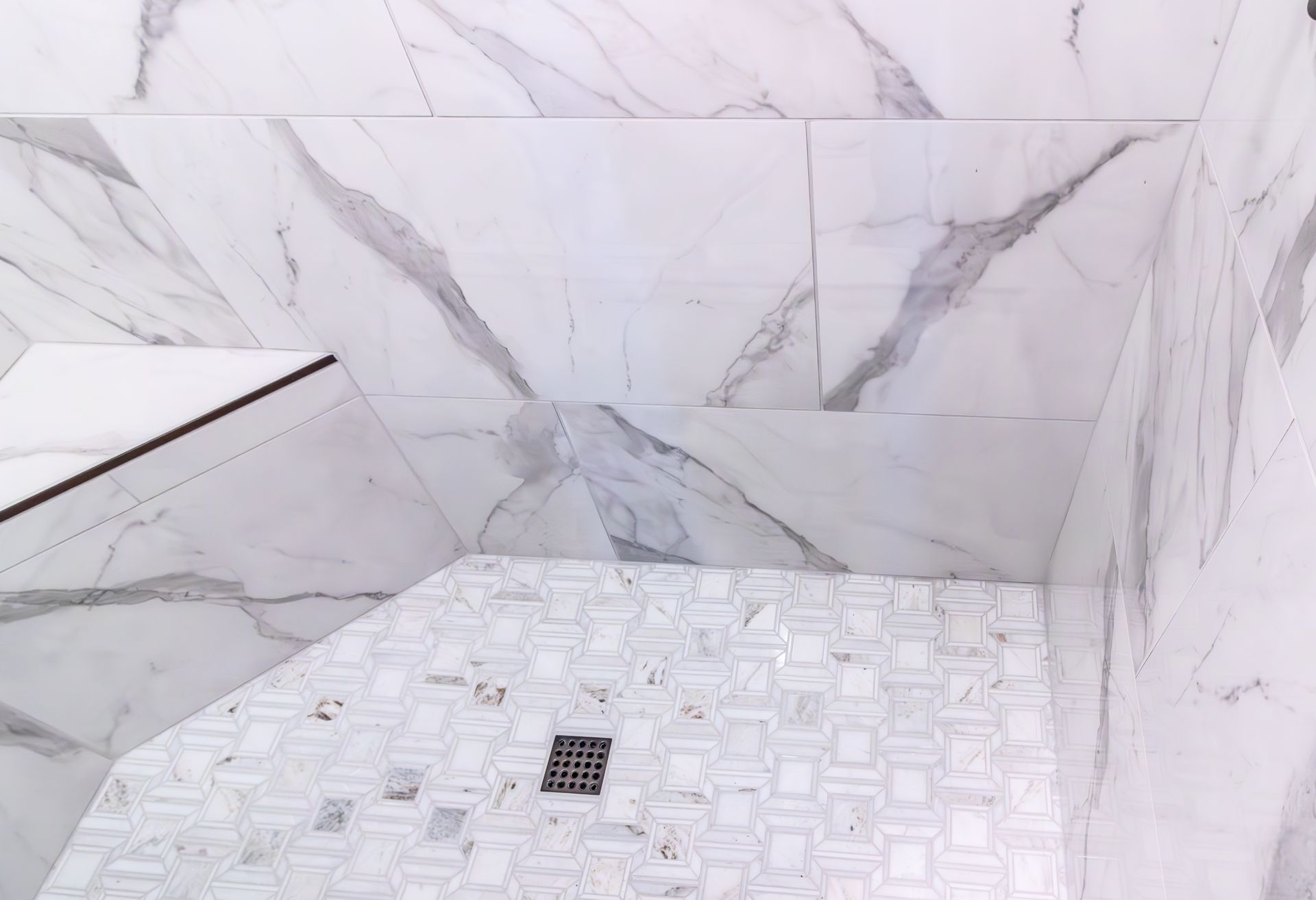 White marble-tiled shower with a square drain and small shelf alcove.