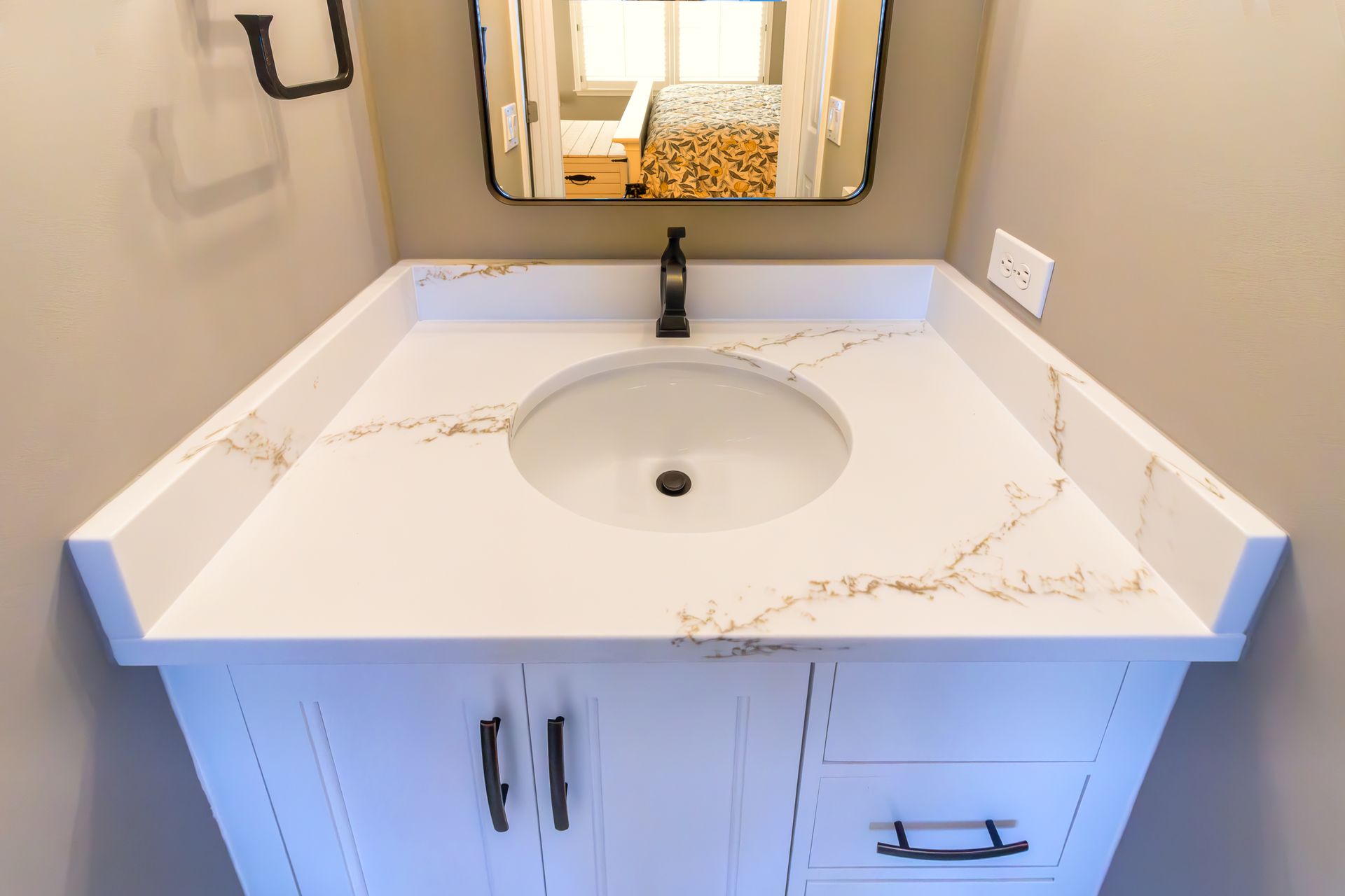 White bathroom vanity with marble countertop, round sink, and wall mirror above it