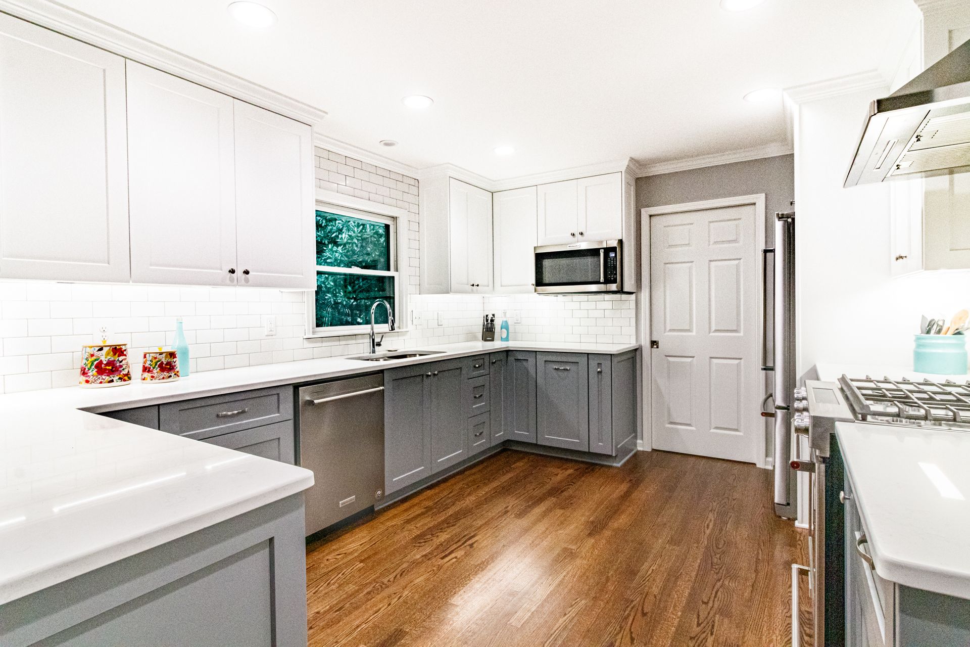 Bright modern kitchen with white cabinets, gray lower cabinets, stainless appliances, and wood floors