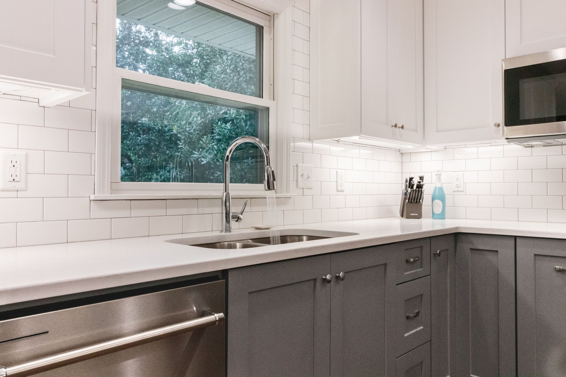Modern kitchen with white cabinets, gray lower cabinets, stainless appliances, and a window over the sink