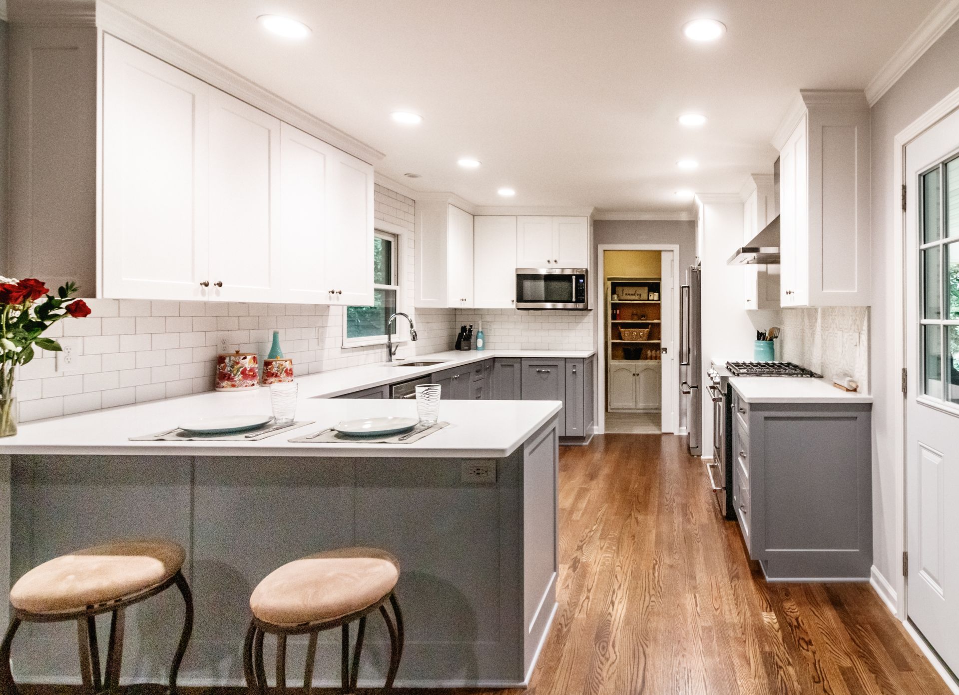 Bright modern kitchen with white cabinets, gray island, wood floors, and two stools