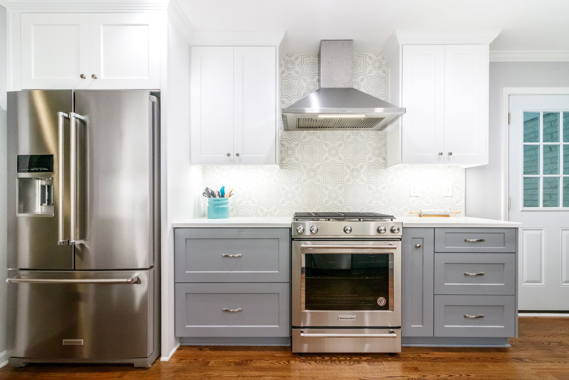 Modern kitchen with stainless steel appliances, white cabinets, gray lower cabinets, and wood floors