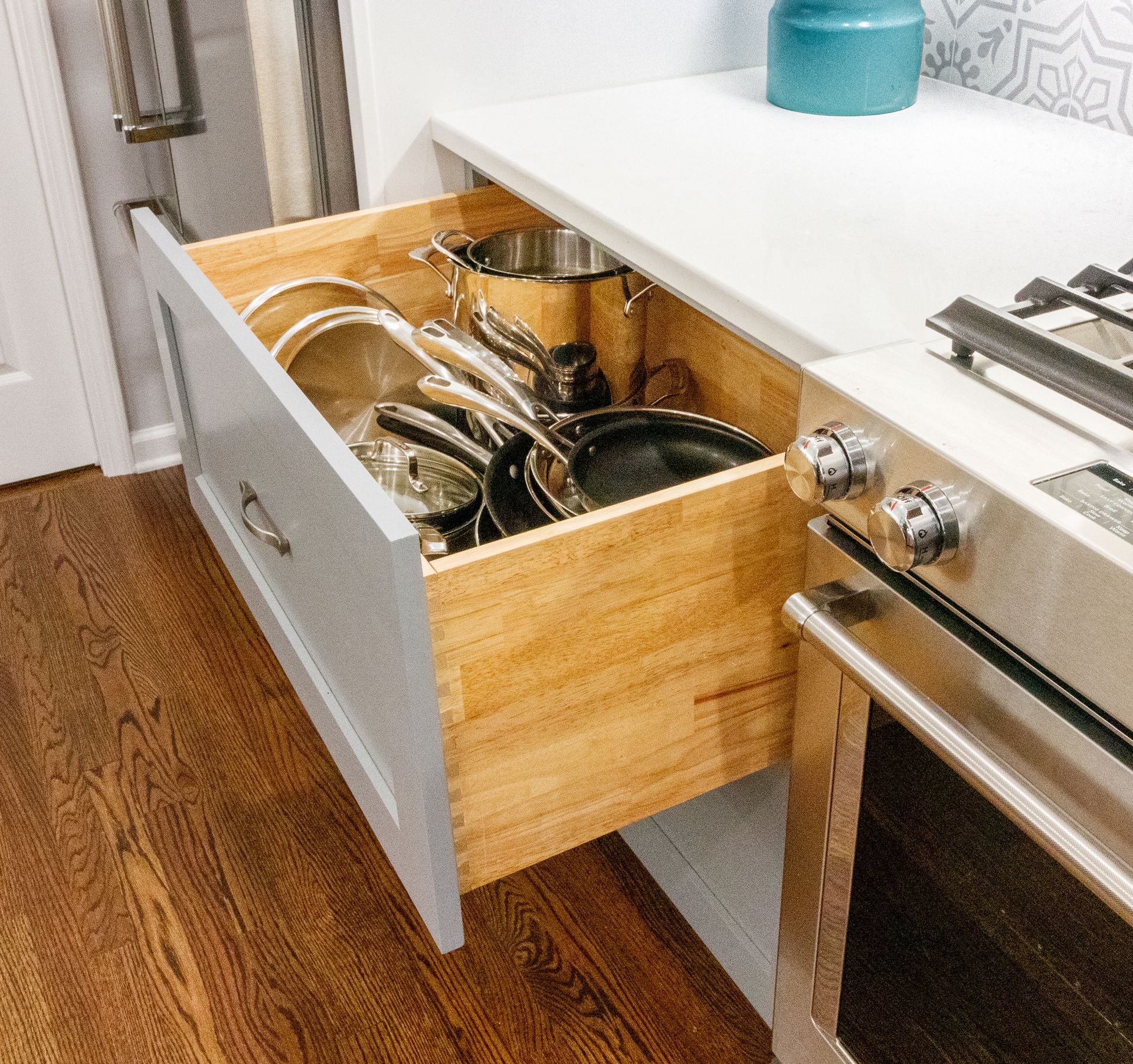 Open kitchen drawer with pots and pans beside a stainless steel stove.