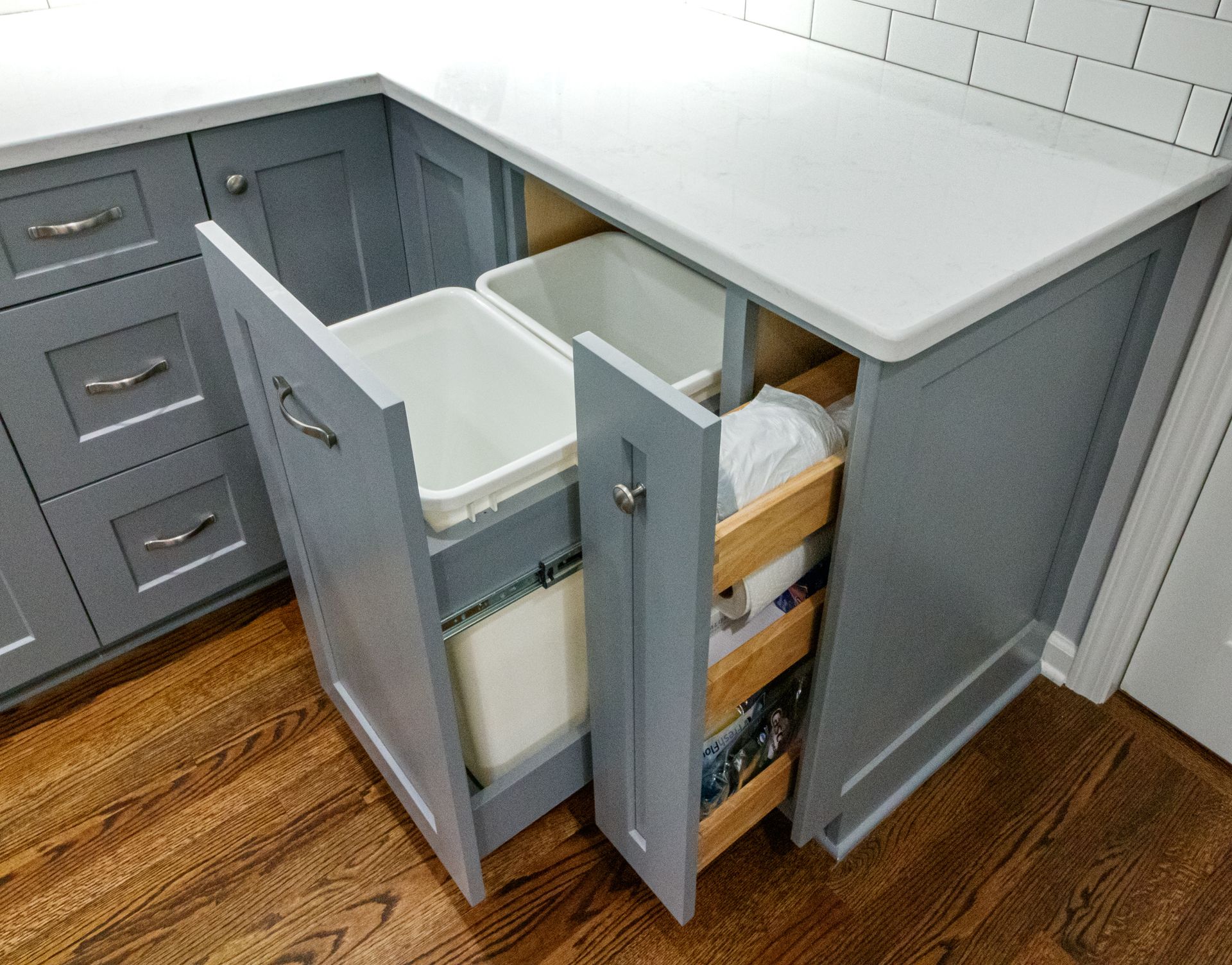 Gray kitchen cabinets with pull-out trash and recycling bins beneath a white countertop