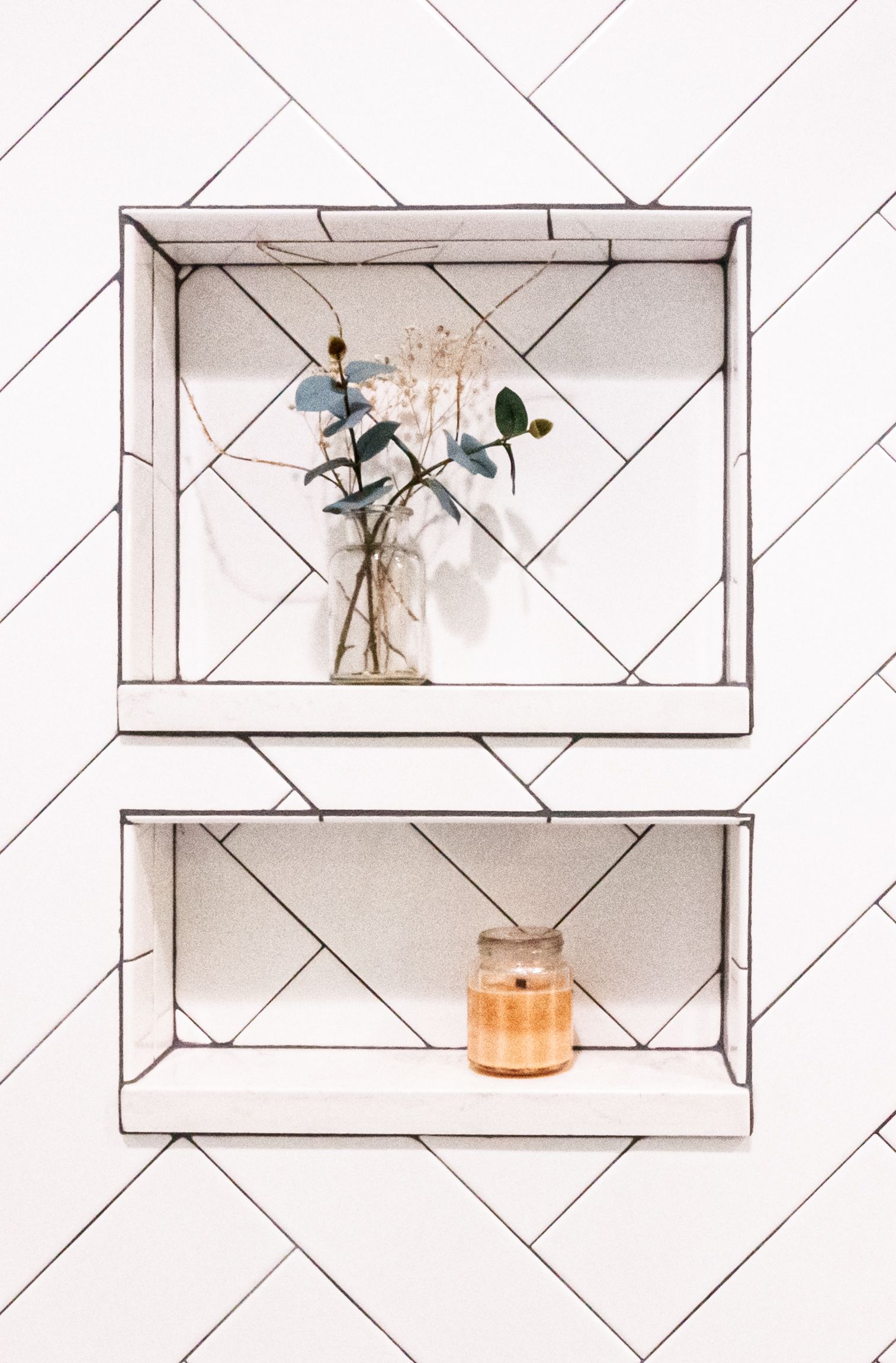 Minimal wall shelves with a small vase and a candle against a white tiled wall