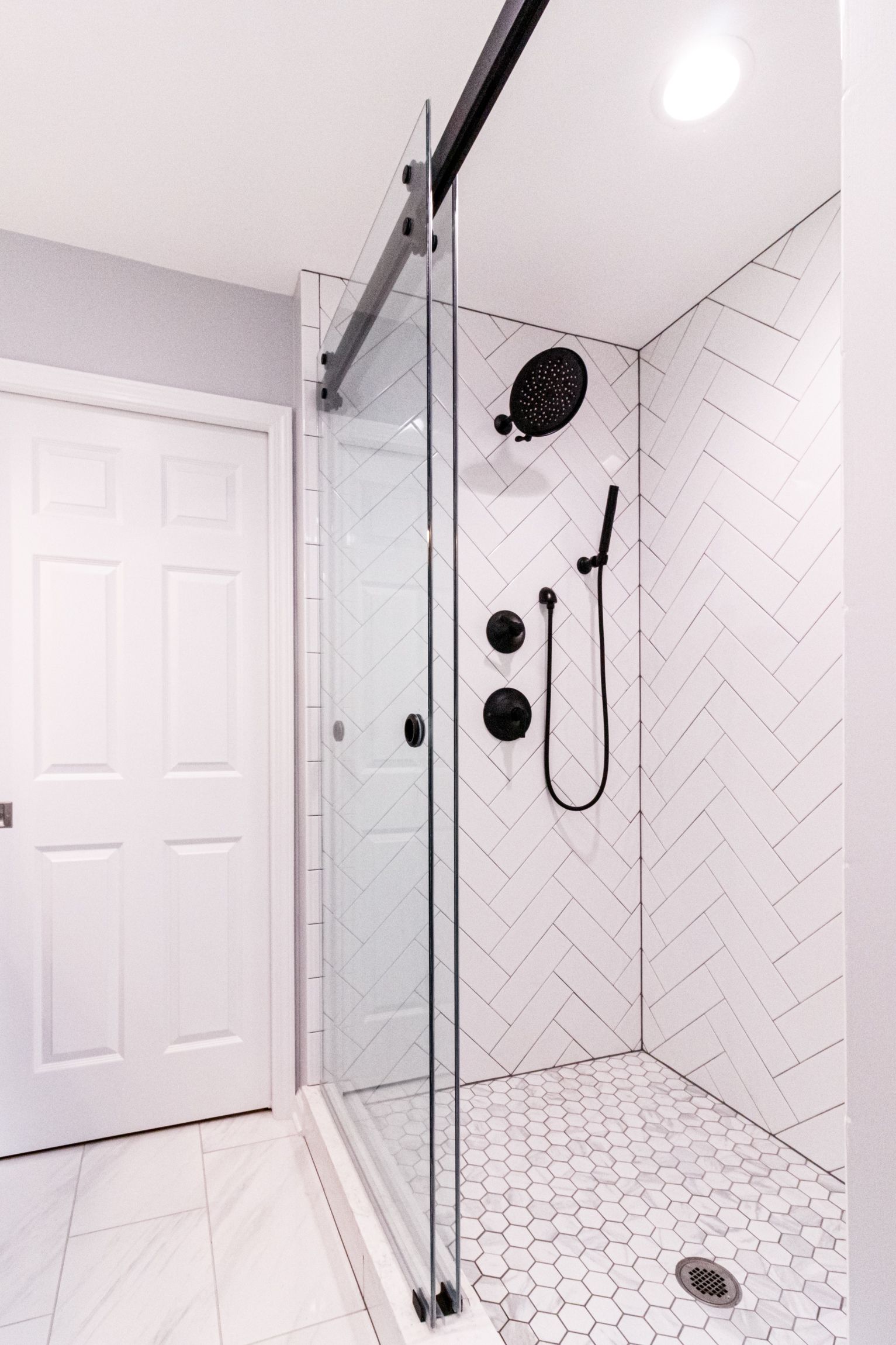 Glass-enclosed white tile shower with black fixtures and a sliding door in a bright bathroom