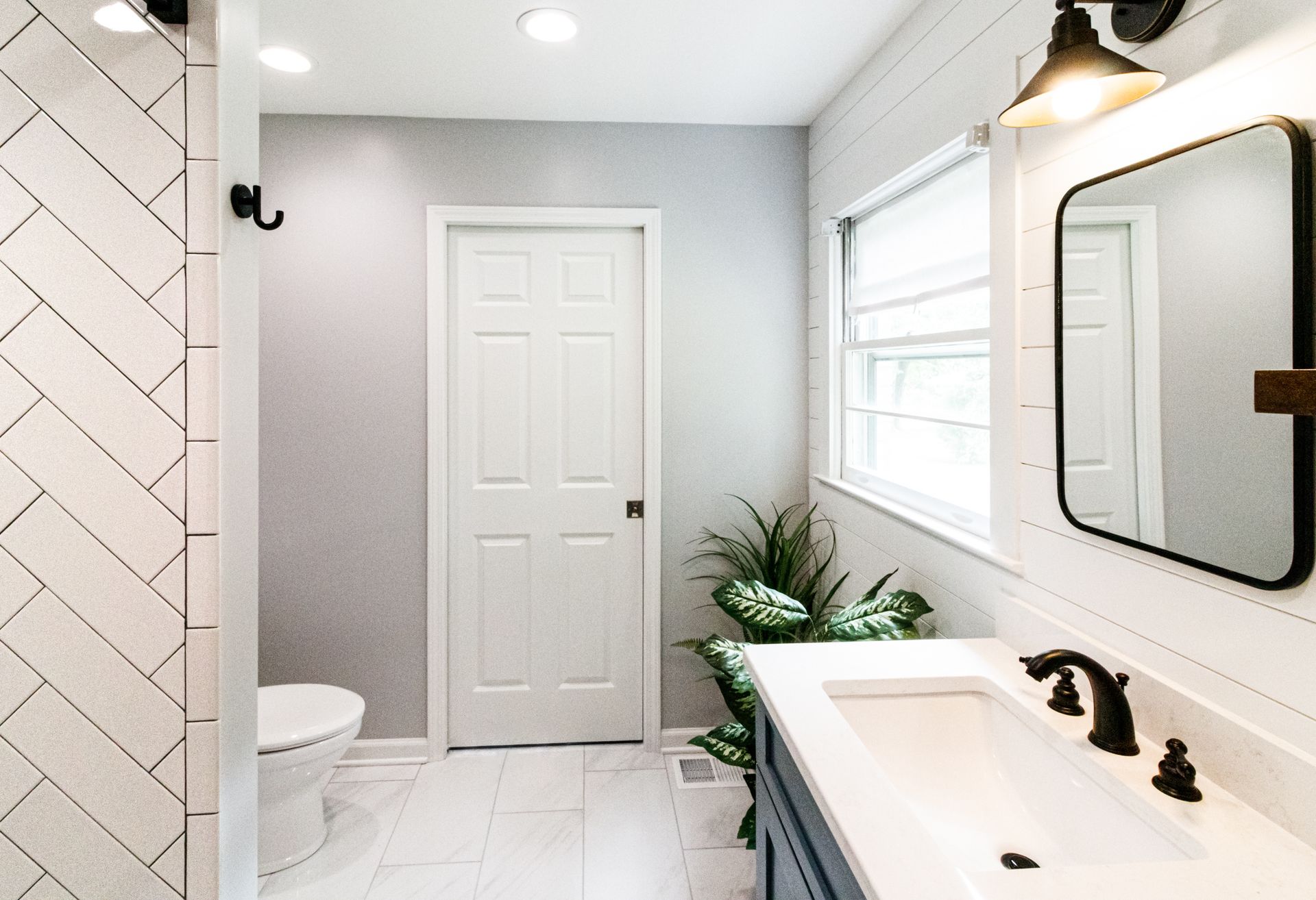 Bright modern bathroom with white tiles, black fixtures, a vanity, mirror, and a potted plant