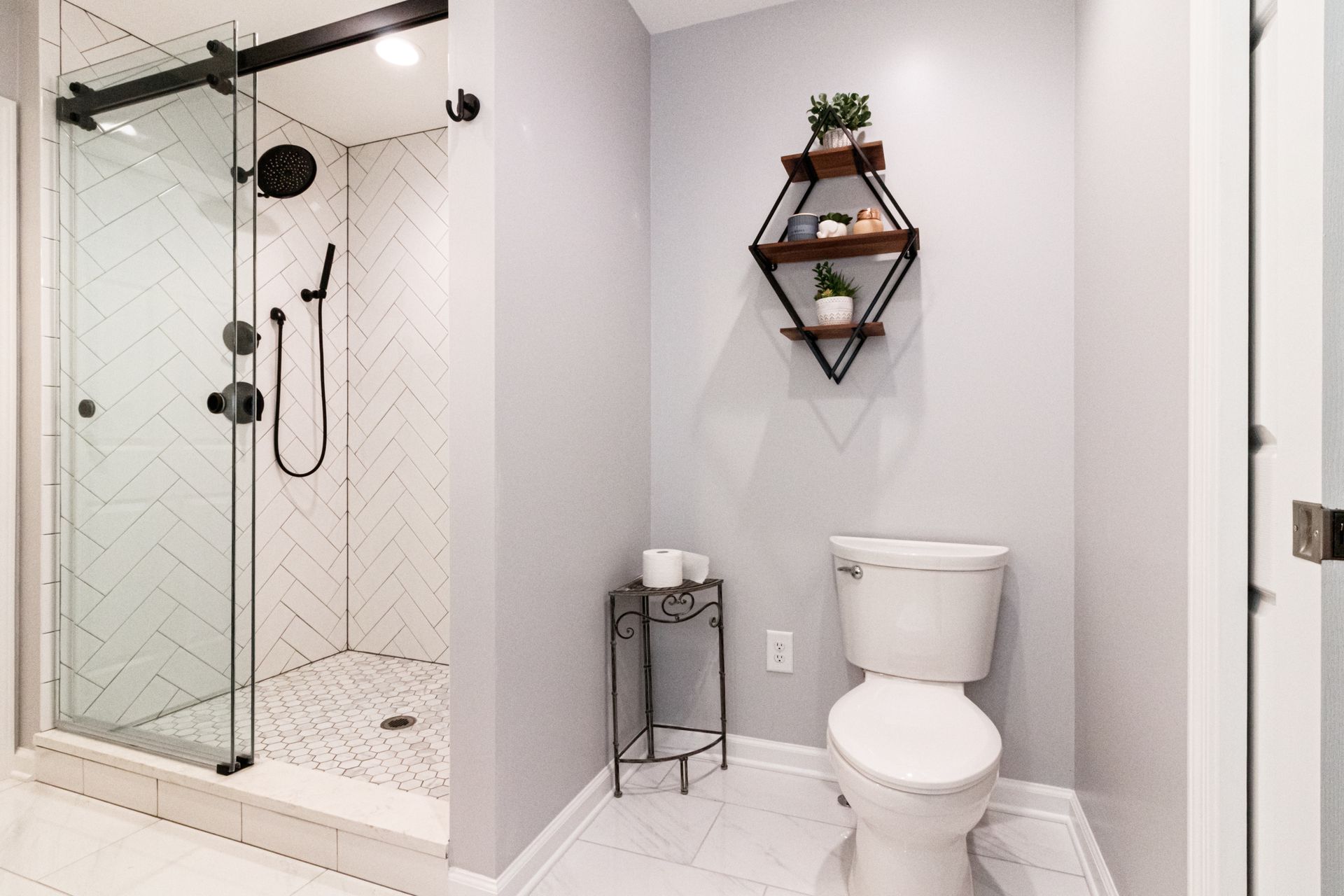 Modern white bathroom with glass shower, toilet, wall shelf, and small plant decor
