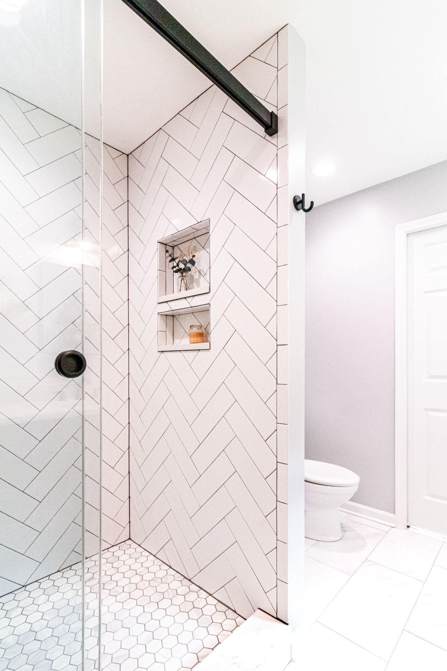 Modern white tiled shower with glass door and a visible toilet in the bathroom.