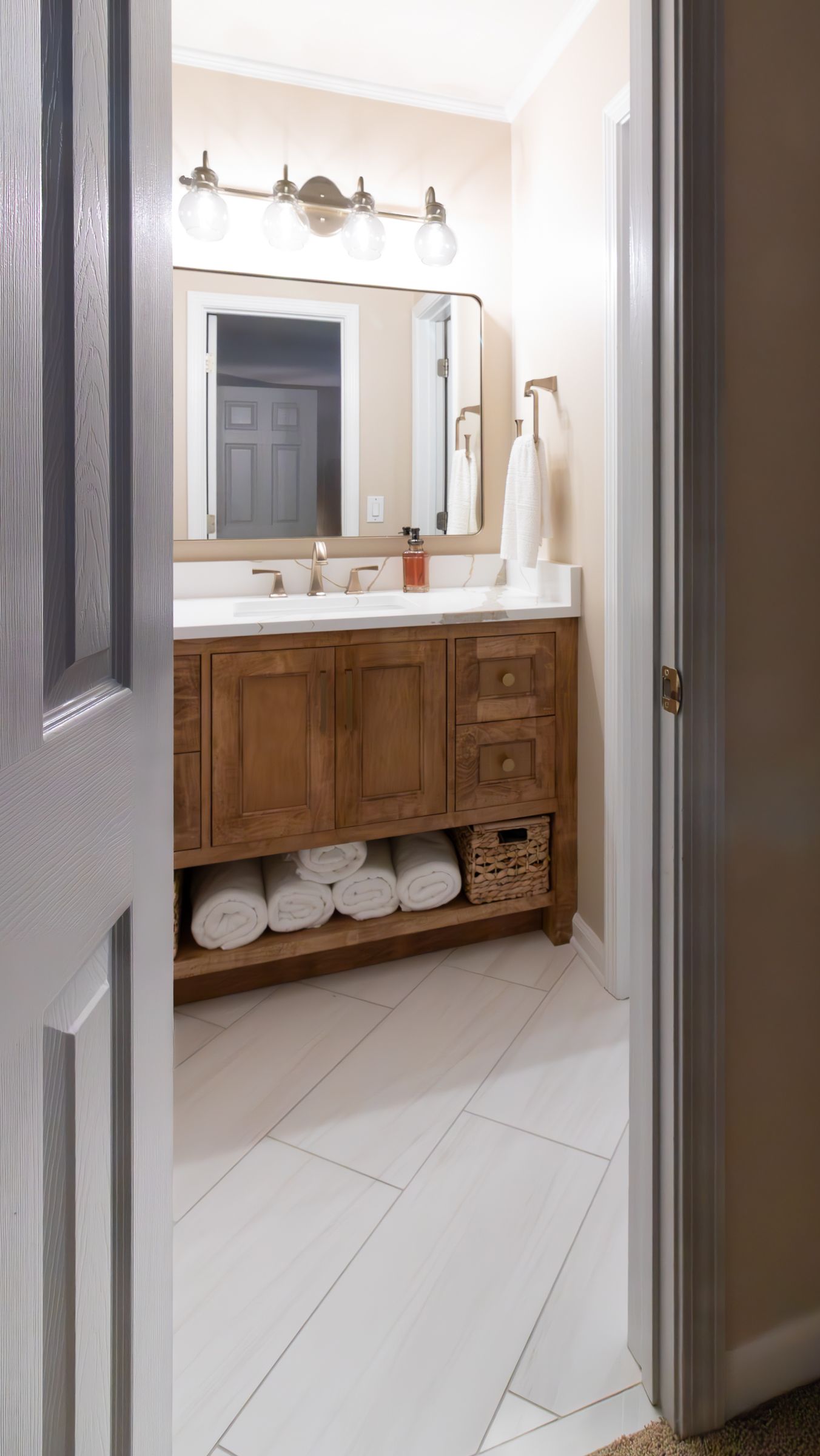Bathroom vanity with wood cabinet, mirror, lights, and neatly folded towels underneath.