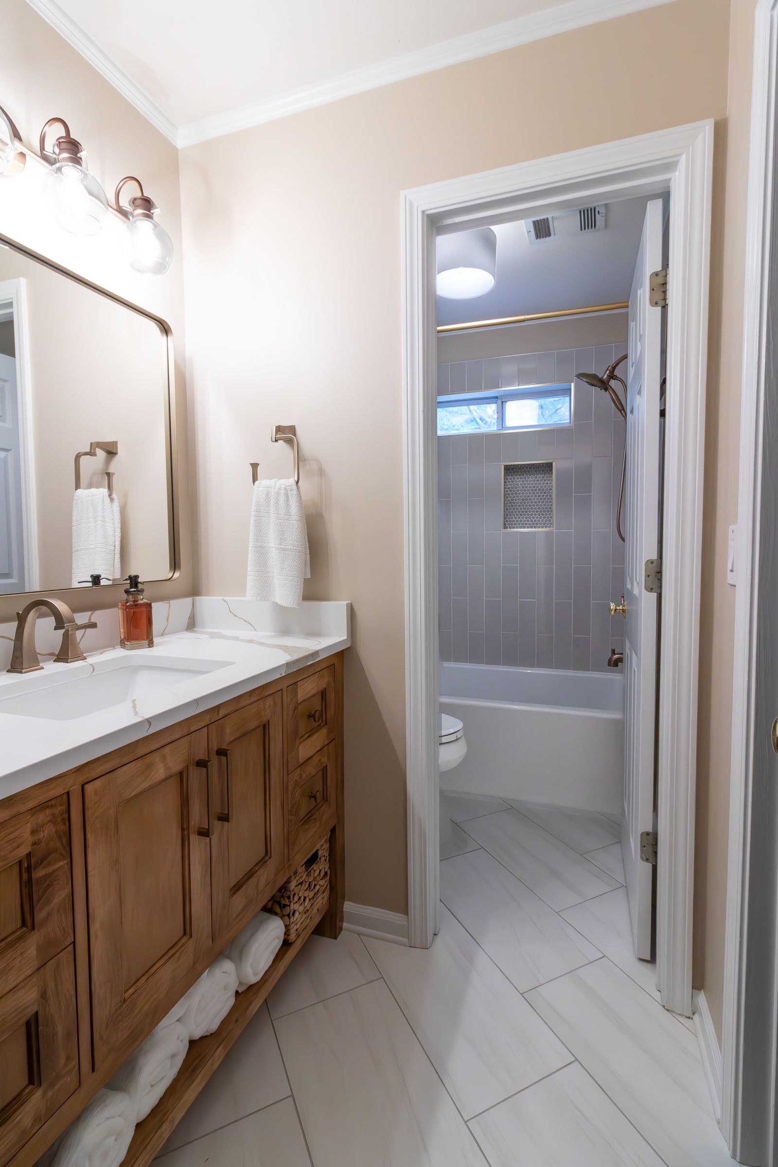 Bathroom with wood vanity, white sink, mirror, and shower visible through the doorway.