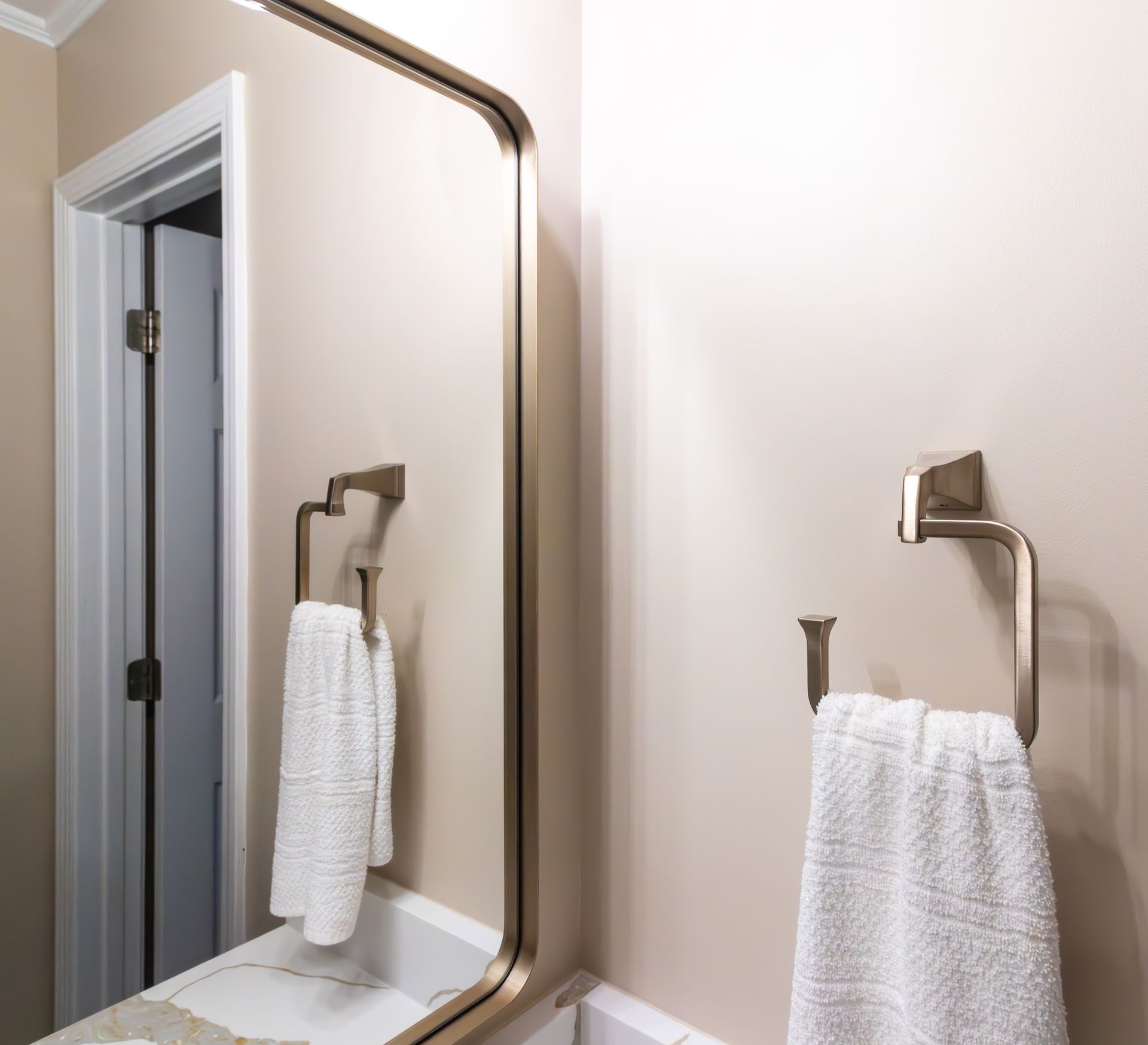 Bathroom mirror reflecting white towels on chrome hooks against beige walls.