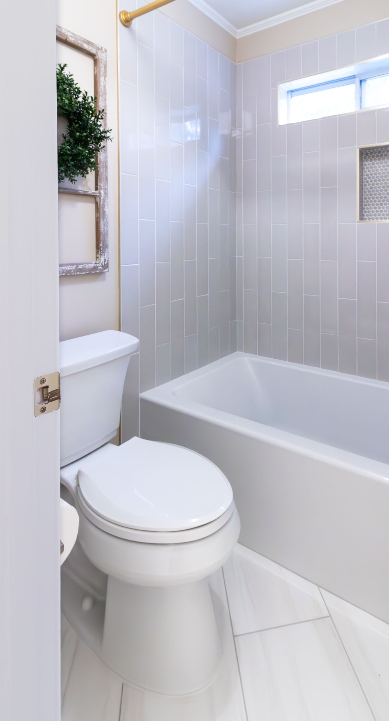 Small white bathroom with a toilet, bathtub, and tiled shower wall with a high window.