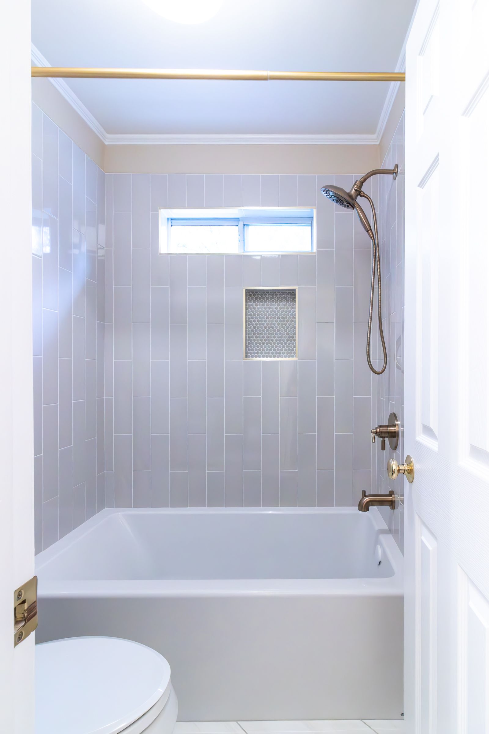 Small white bathroom with a bathtub, shower head, tiled walls, and a toilet partially visible.