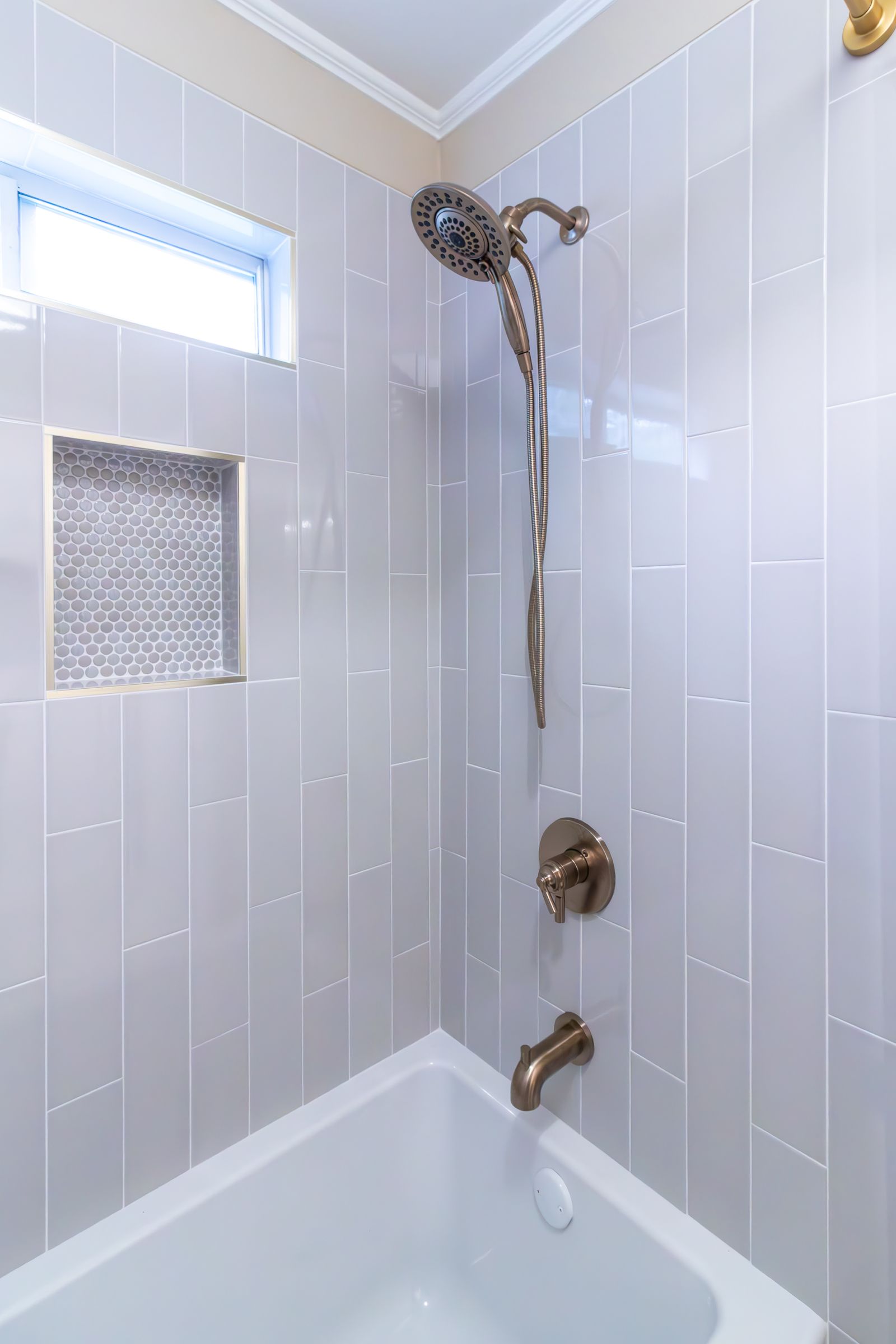 White tiled shower and bathtub with chrome showerhead and frosted window above.
