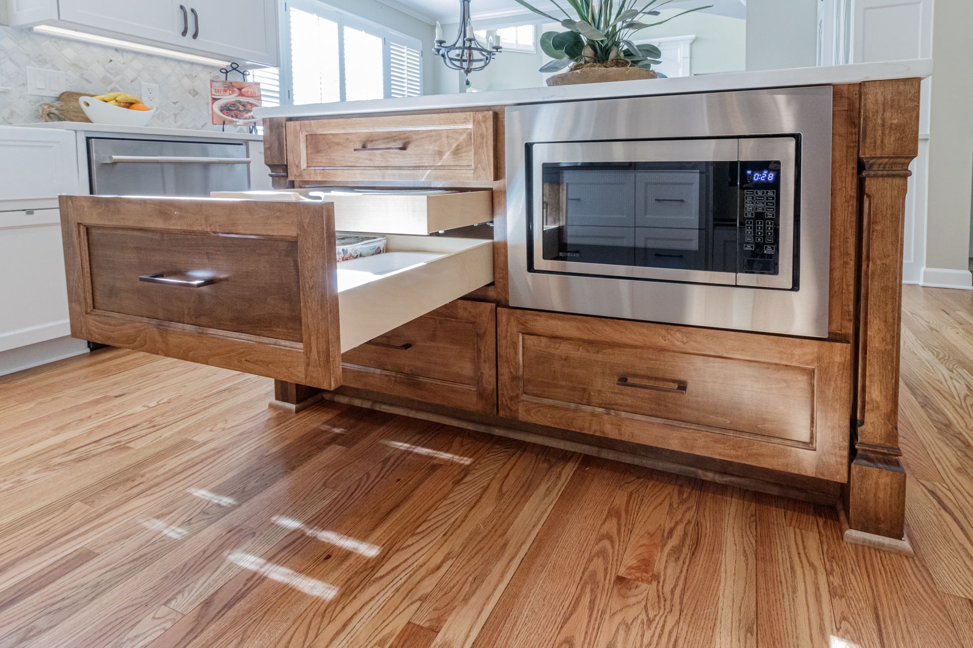 Kitchen island with pull-out drawers and built-in microwave in a bright hardwood-floored kitchen