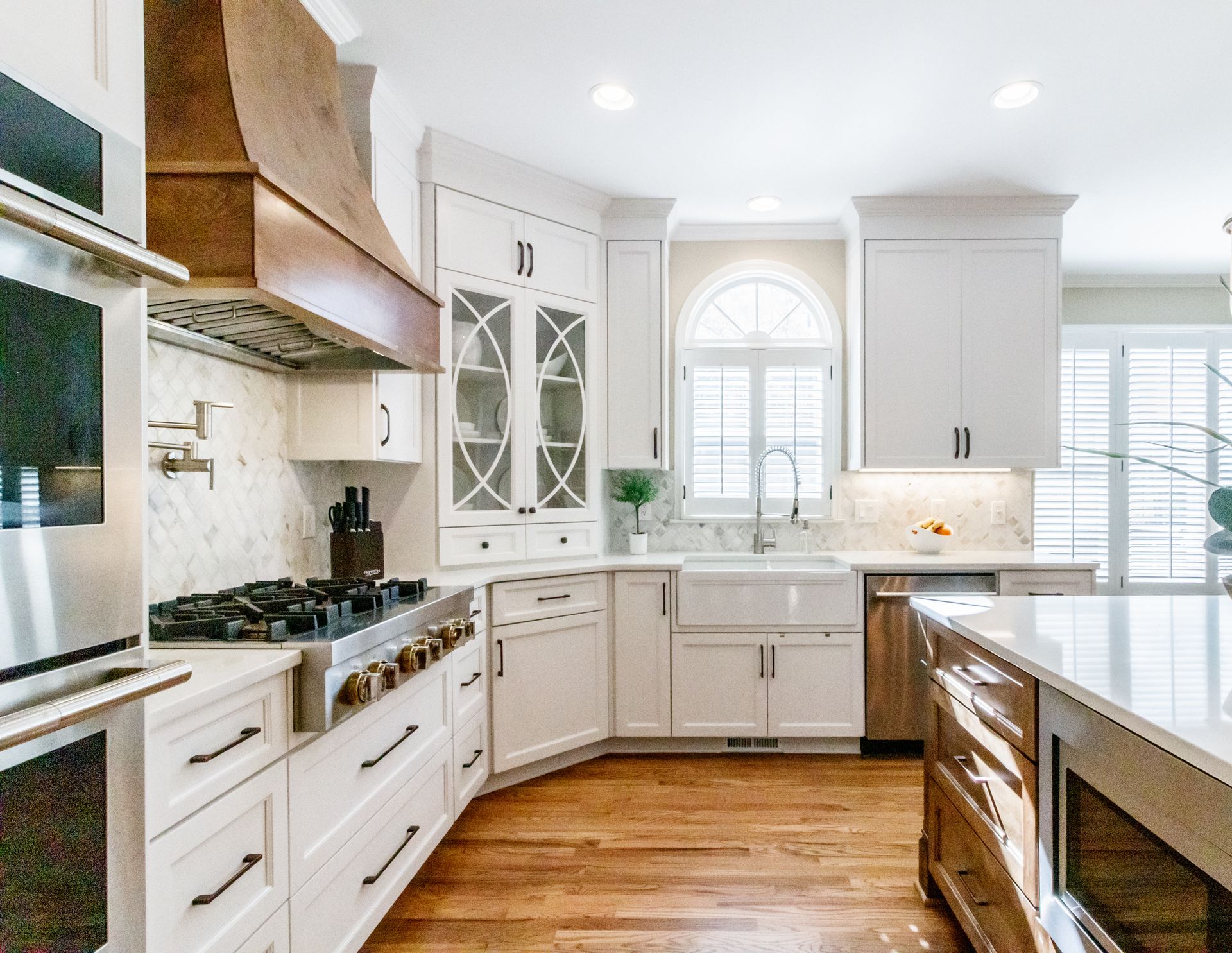 Bright white kitchen with wood floors, marble island, stainless appliances, and large windows