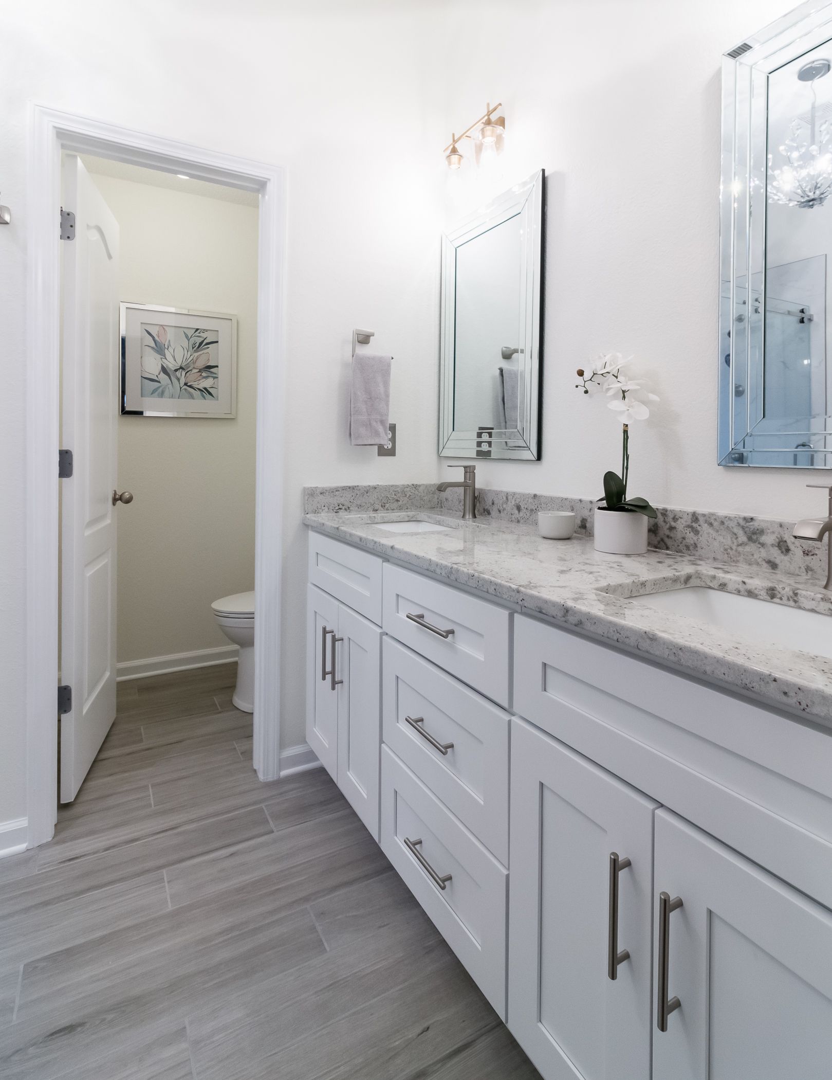 Bright white bathroom with double vanity, marble countertop, mirrors, and an open doorway.