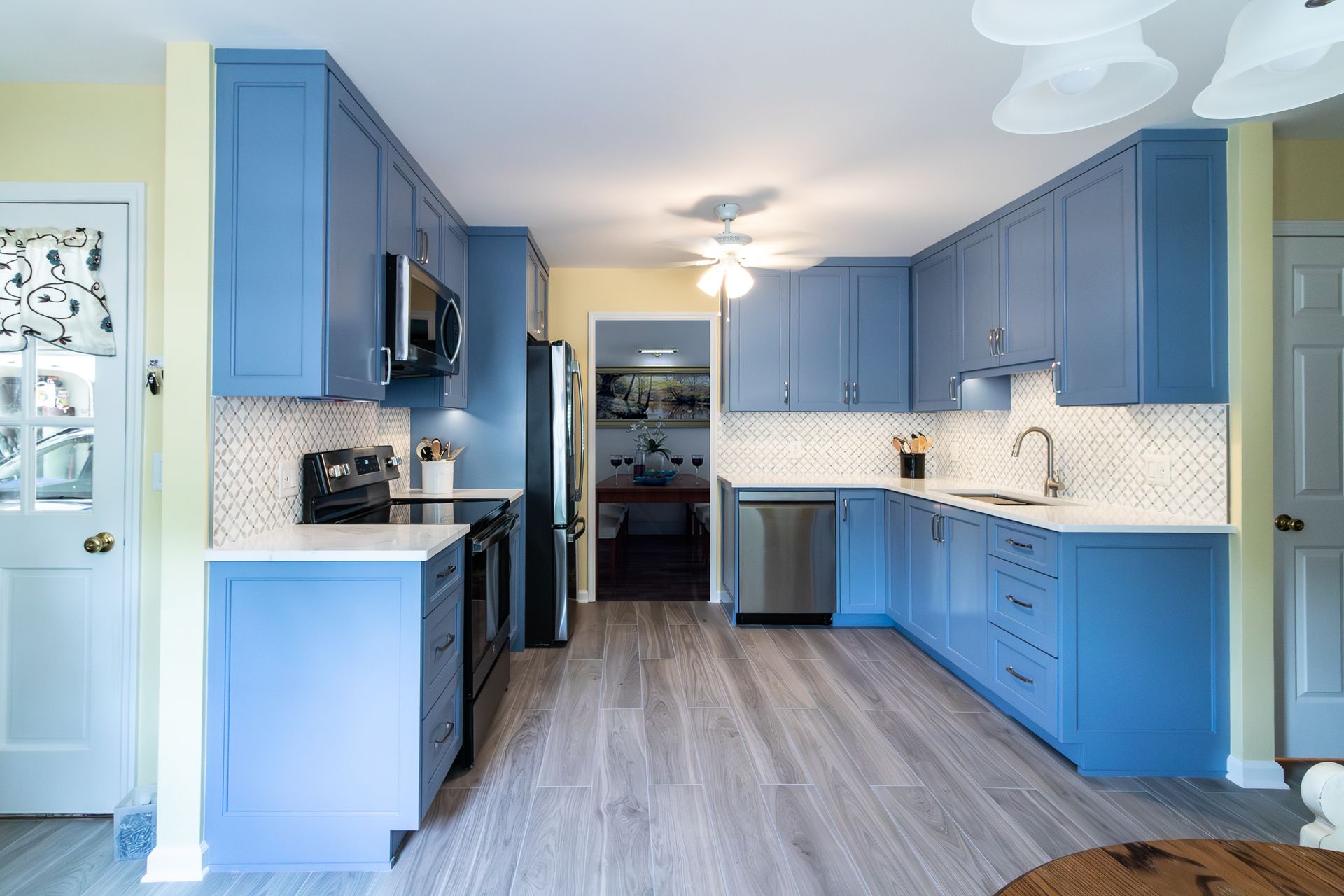 Blue kitchen with white backsplash, stainless appliances, and wood-look flooring