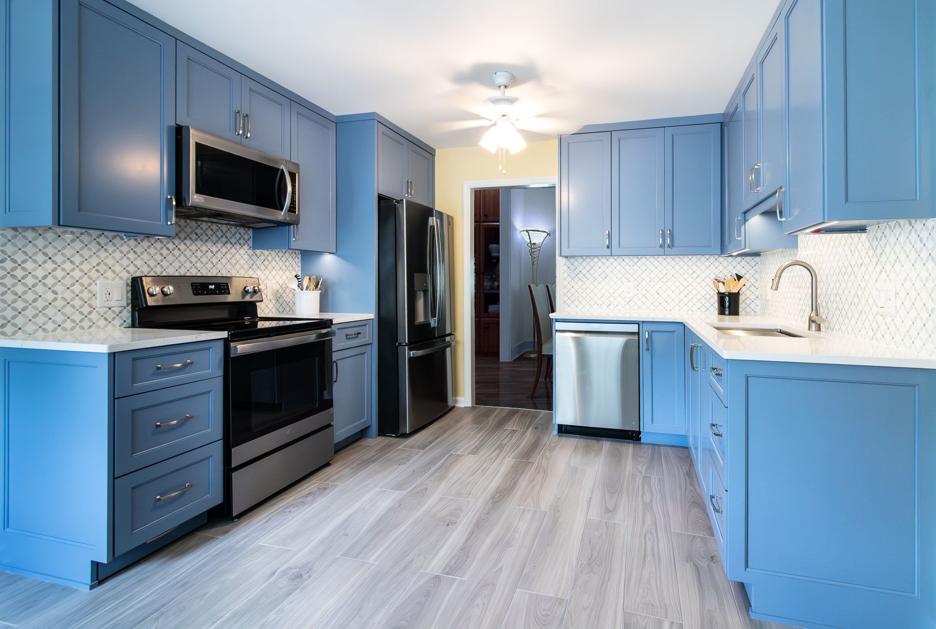 Bright blue kitchen with stainless appliances, white countertops, and light wood flooring