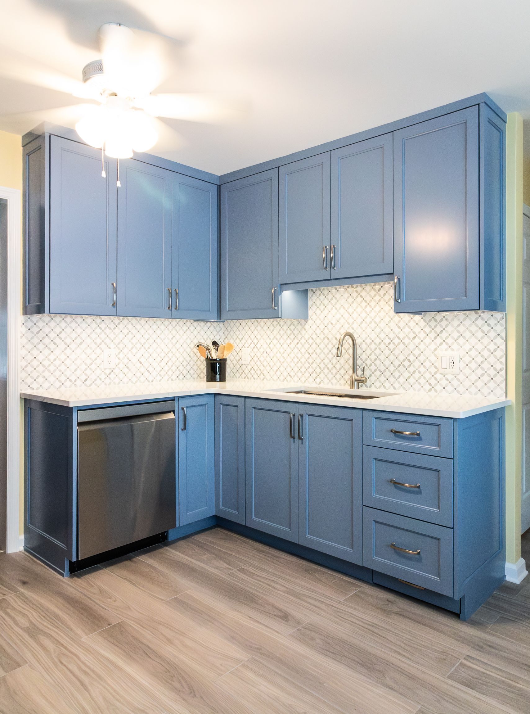 Blue kitchen with white backsplash, stainless dishwasher, and wood-look flooring