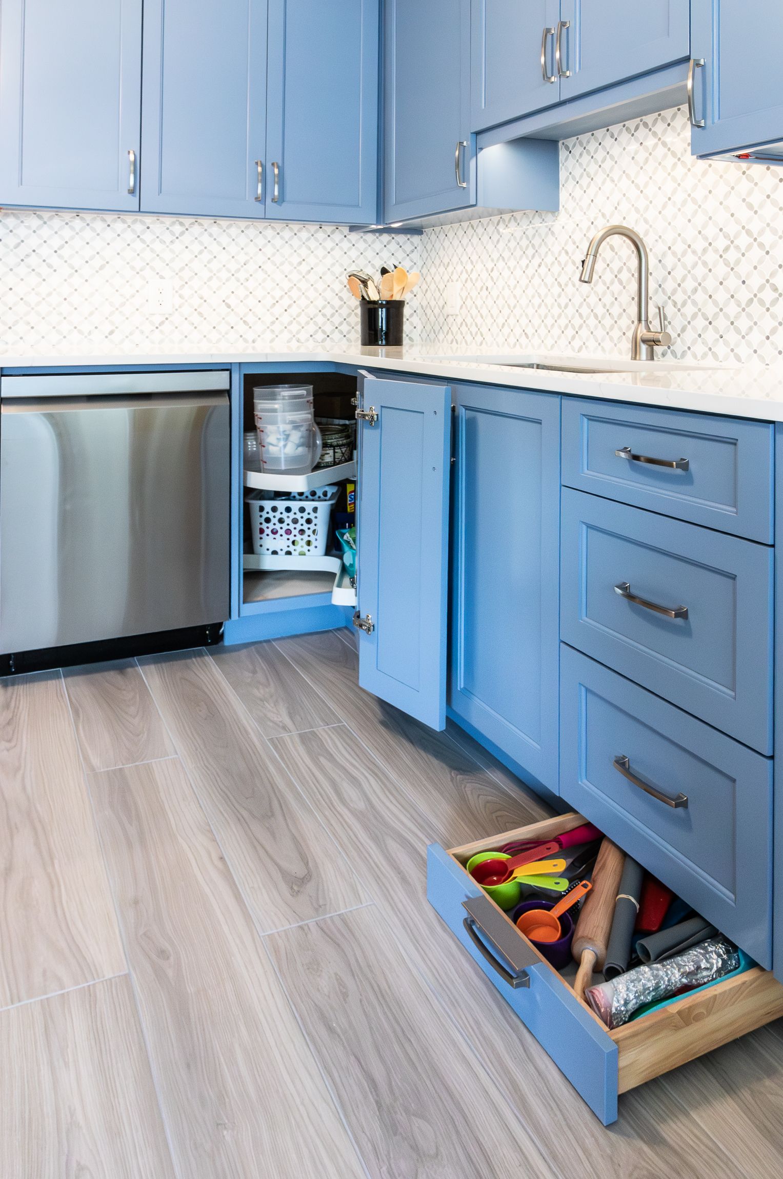 Modern blue kitchen with open cabinets and drawers, stainless dishwasher, and light wood floor