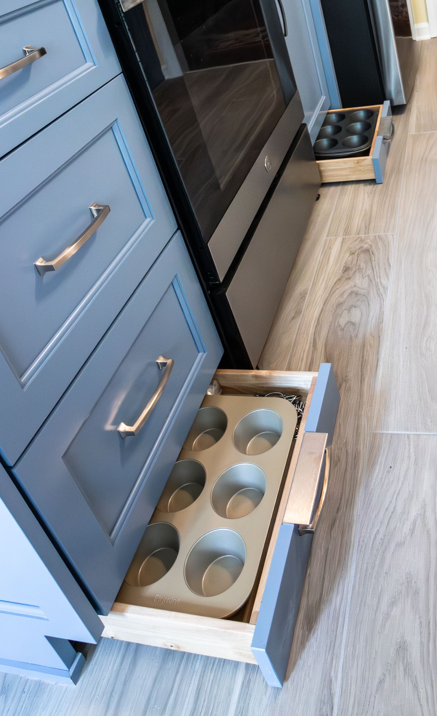 Kitchen drawers with built-in metal can holders next to an oven on a wood floor.