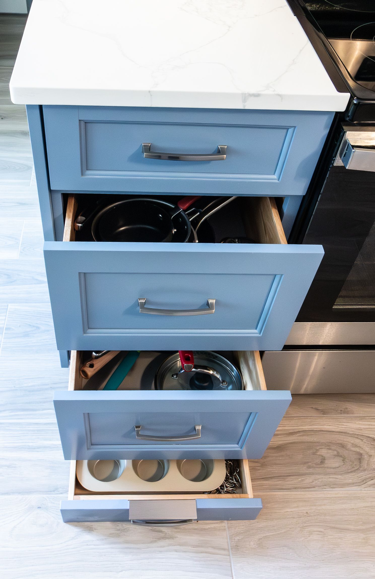 Blue kitchen drawer unit with drawers open, showing stored utensils and bottles inside