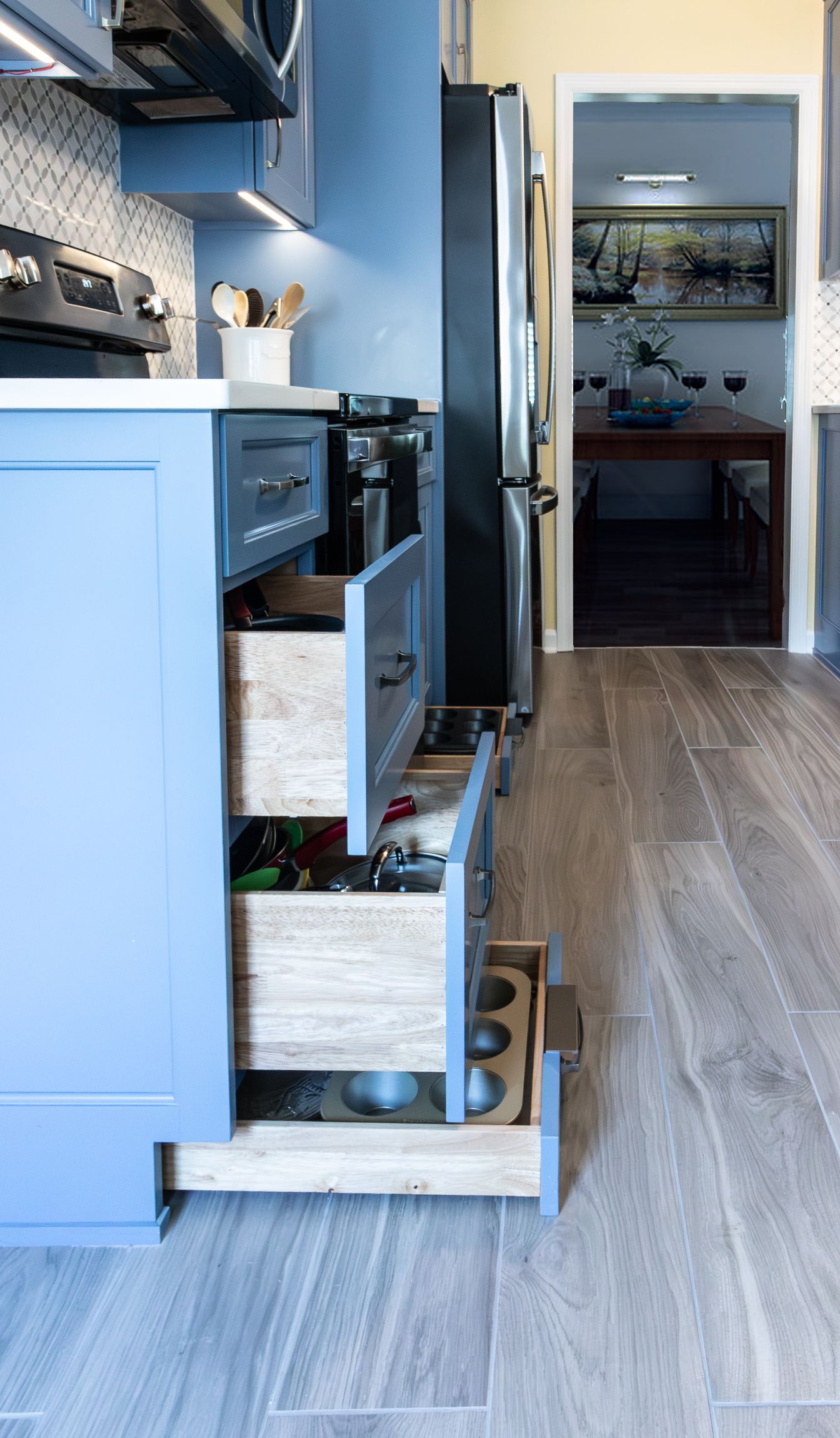 Blue kitchen with drawers open, showing pull-out pantry bins and a doorway to a small pantry or utility room.