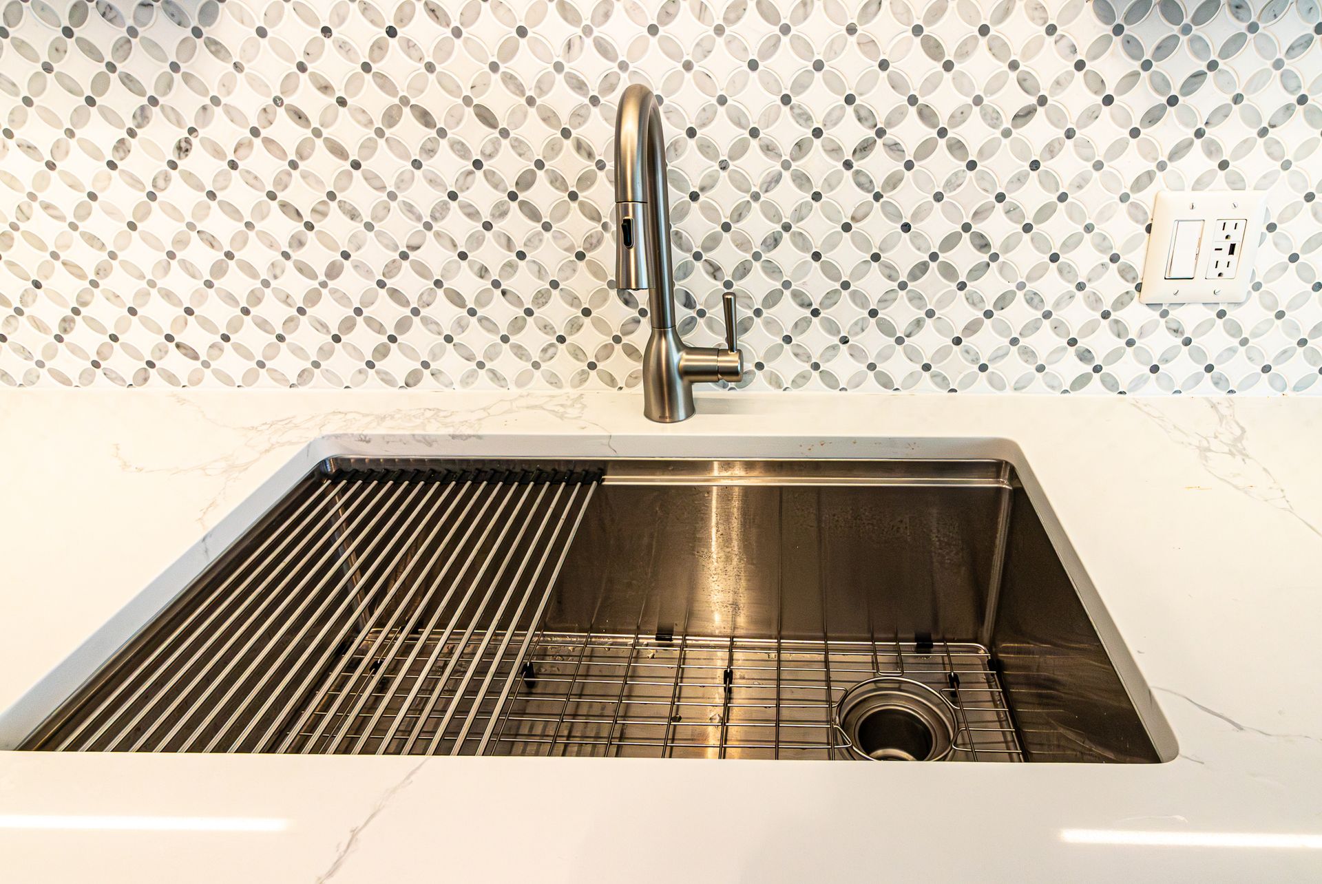 Modern kitchen sink with chrome faucet and stainless steel basin under patterned tile backsplash