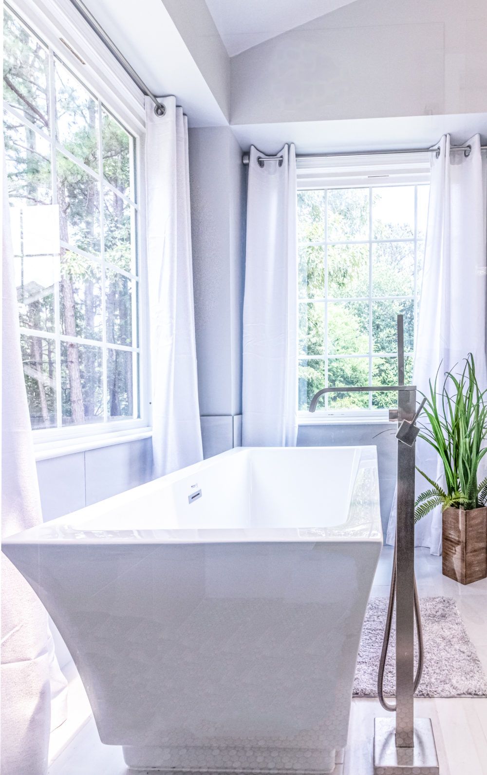 Bright modern bathroom with a freestanding white tub beside large windows and a potted plant