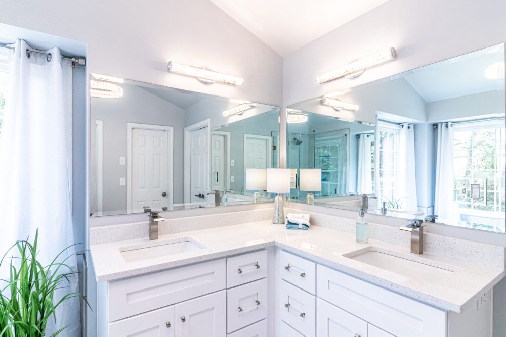 Bright bathroom vanity with double sinks, large mirrors, white cabinets, and light blue walls