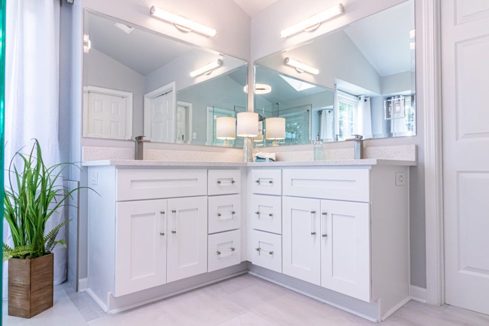 Bright white bathroom vanity with double sinks, large mirrors, and a potted plant in a modern interior