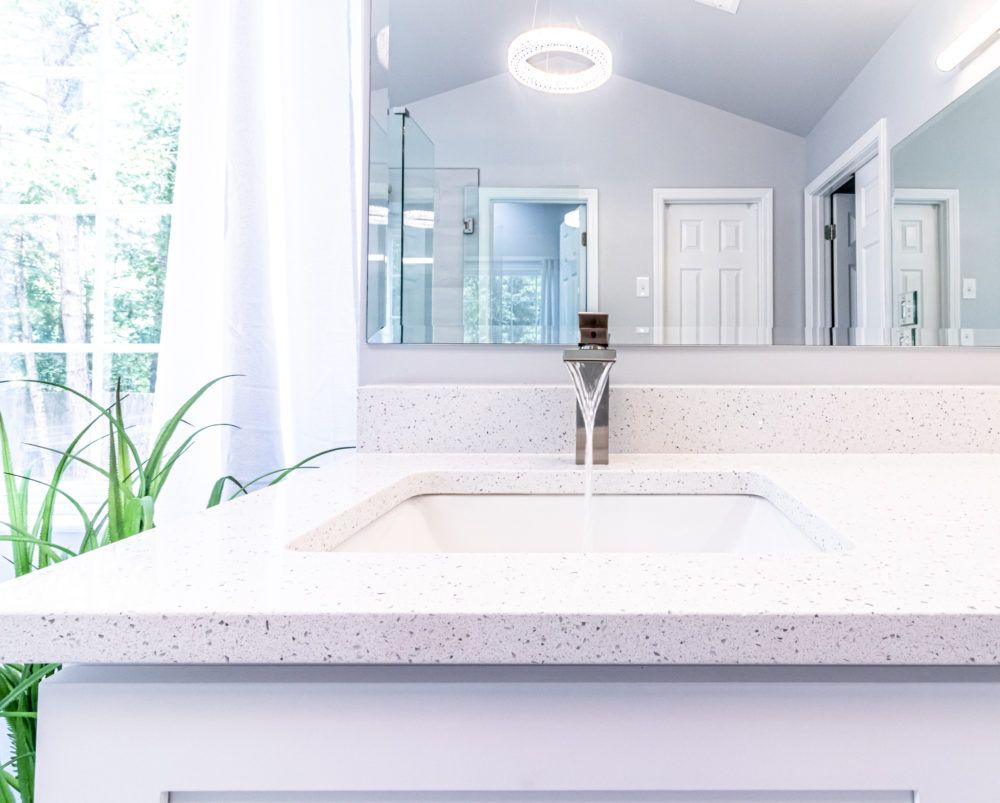 Bright modern bathroom vanity with white countertop, mirror, and sunlight by a window