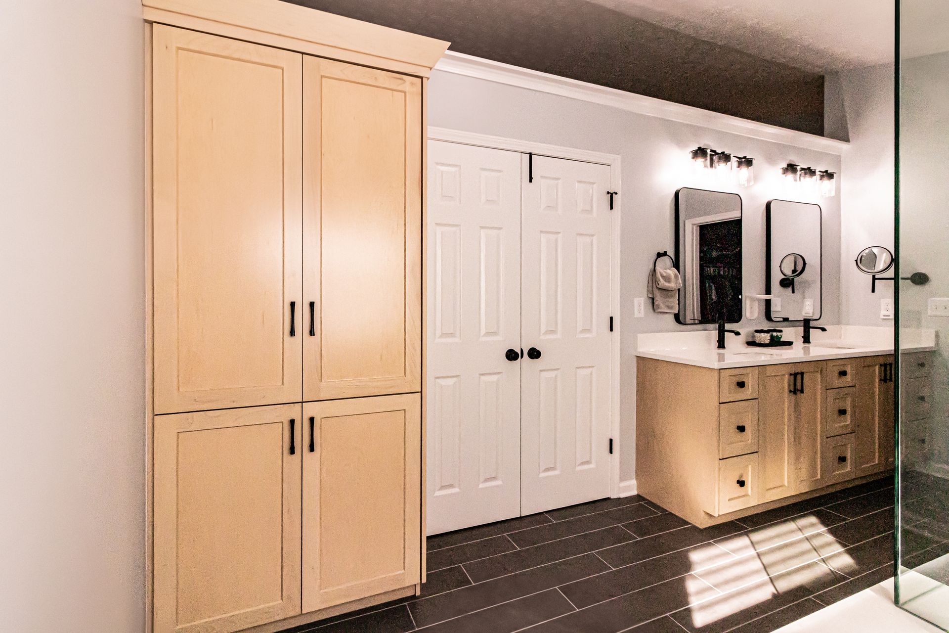 Bright bathroom with light wood cabinets, white double doors, and a vanity with mirrors and lights.