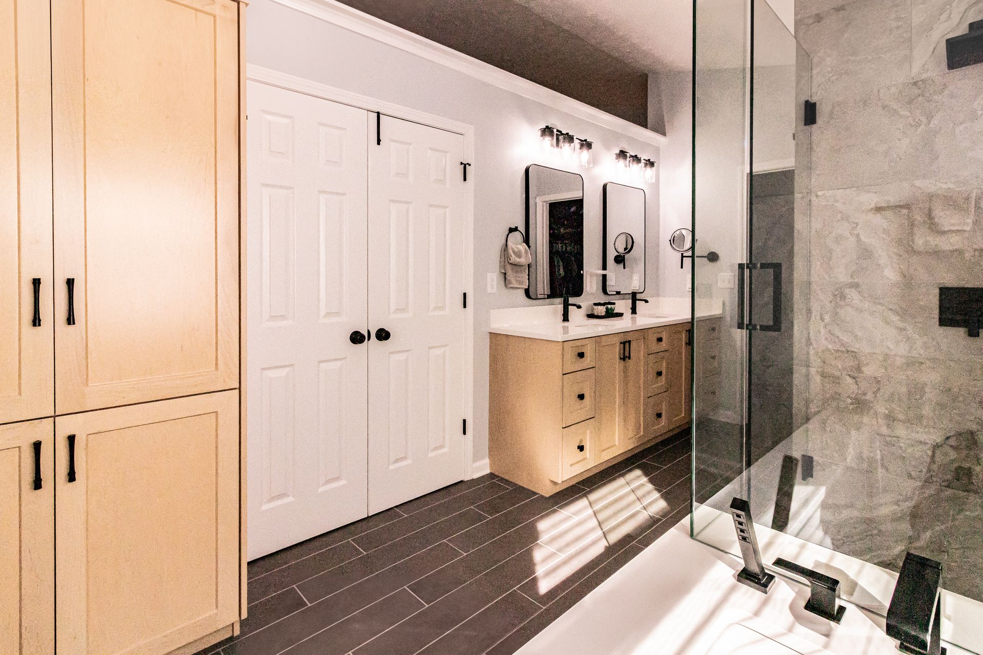 Modern bathroom with double vanity, white doors, and glass shower beside a bathtub.