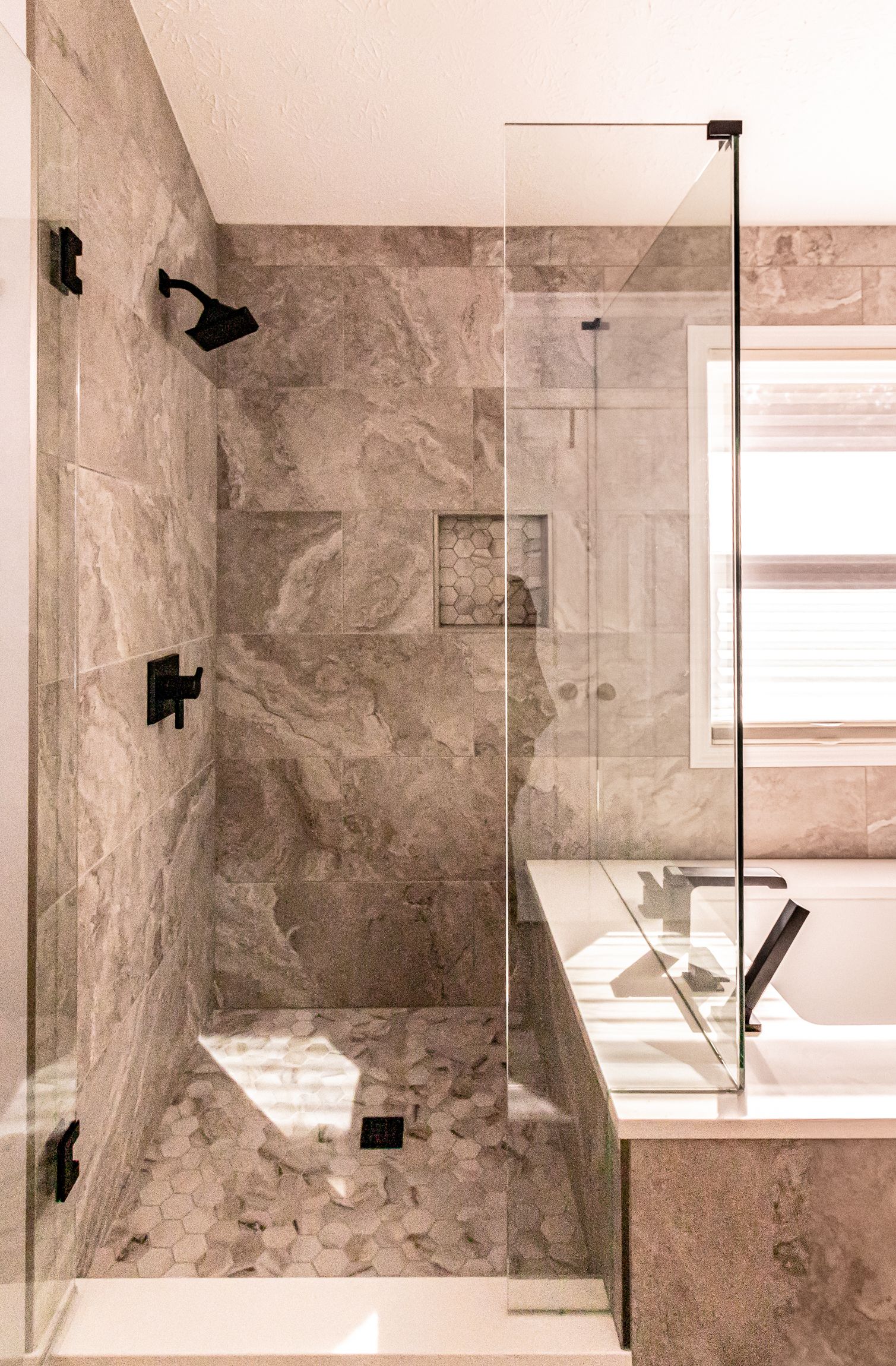 Modern bathroom shower with gray stone tile, glass partition, and window light